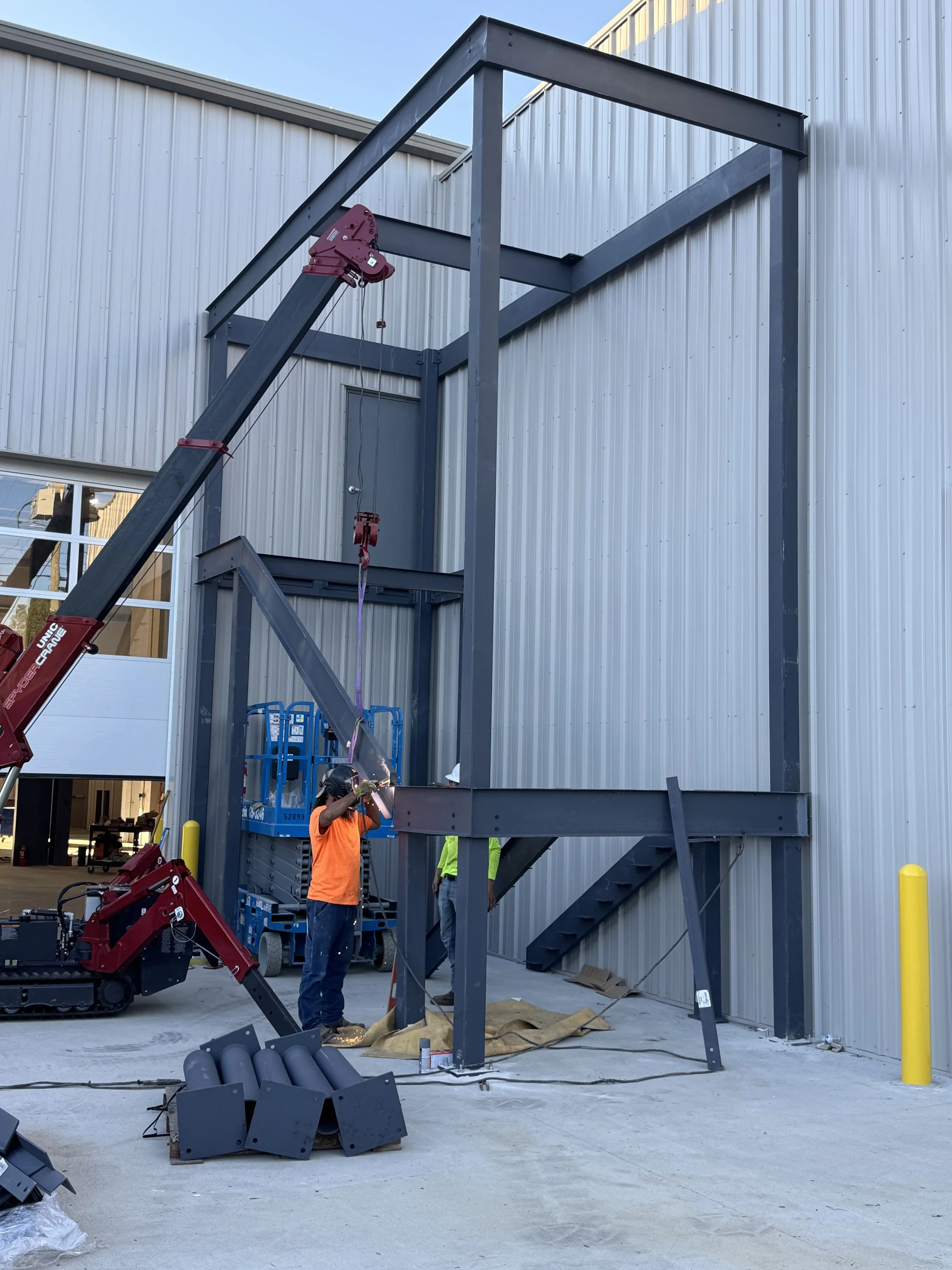 Workers installing a steel structure outside a building with a crane lifting a steel beam.