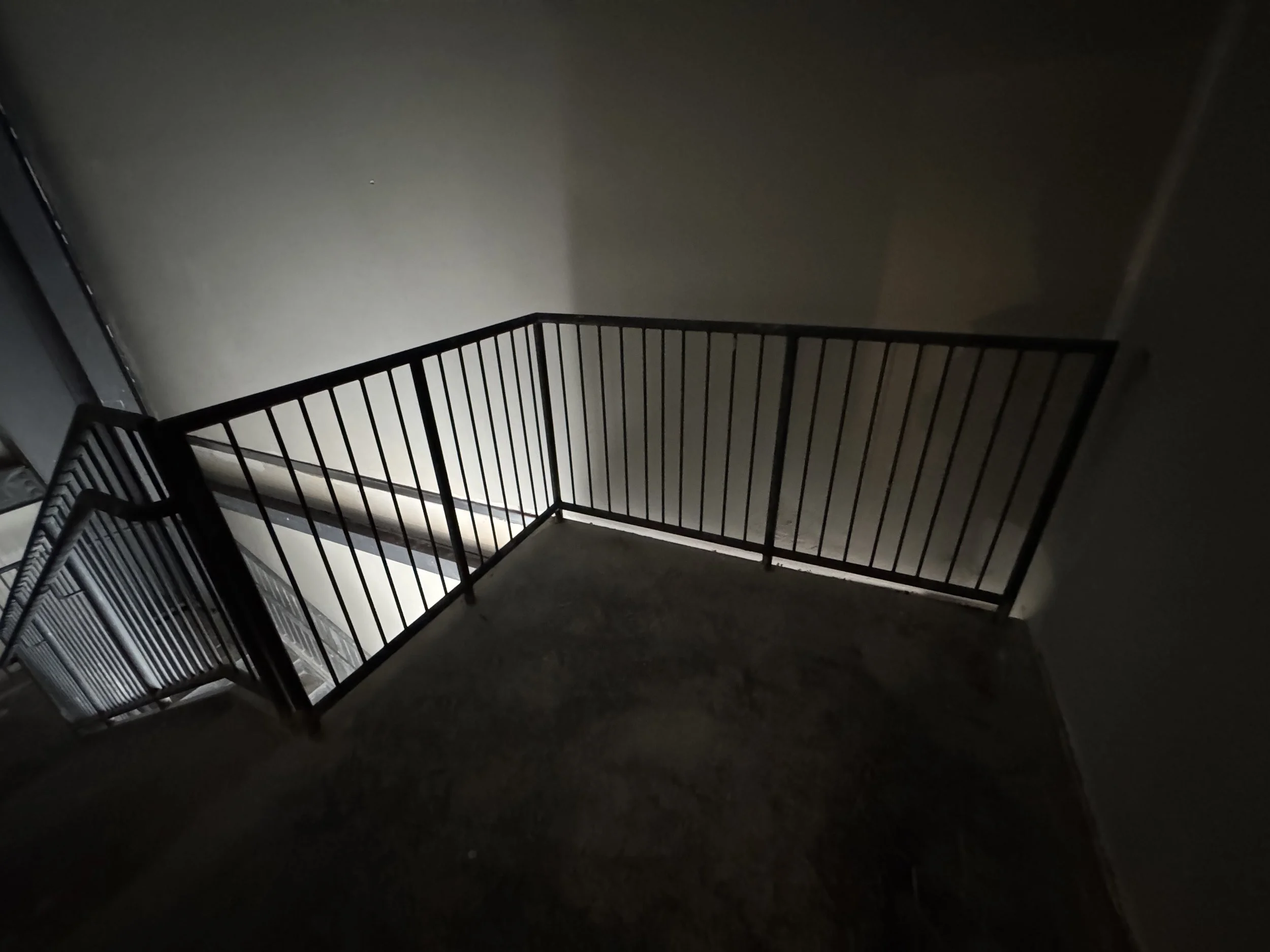 Dark staircase with metal railing leading down to a lower floor, with shadows on the walls from lighting.