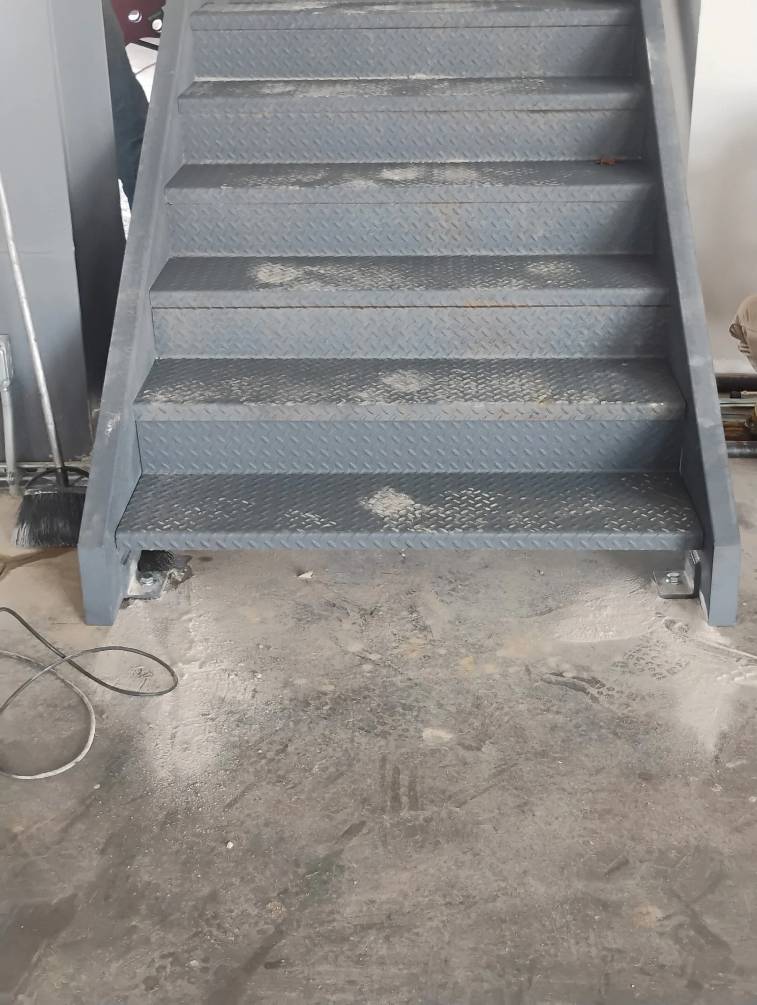 Metal staircase with five steps, located on a dirty concrete floor in an industrial or warehouse setting.