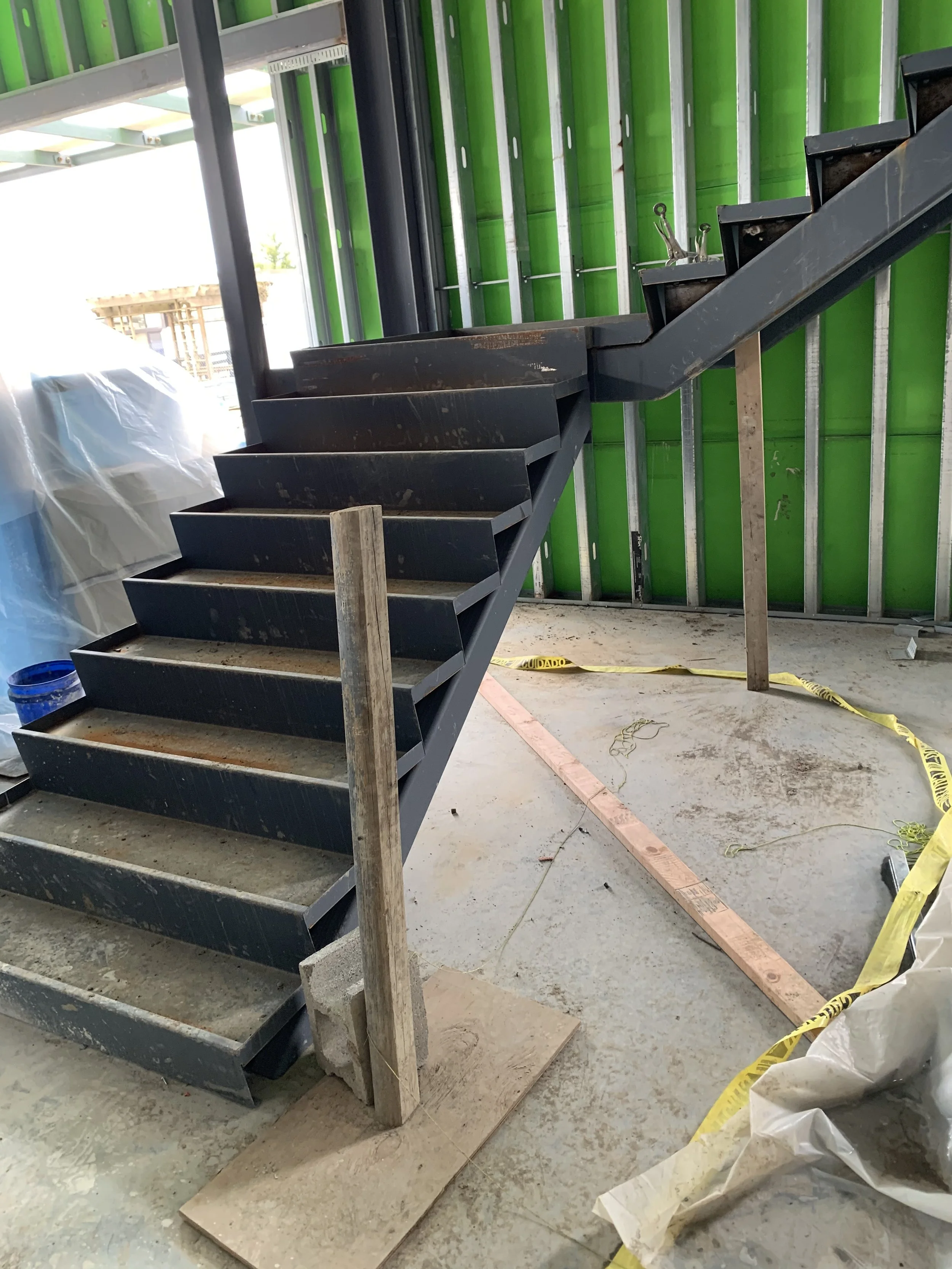 Black metal staircase under construction inside a building with green wall panels, construction materials, and tools around.
