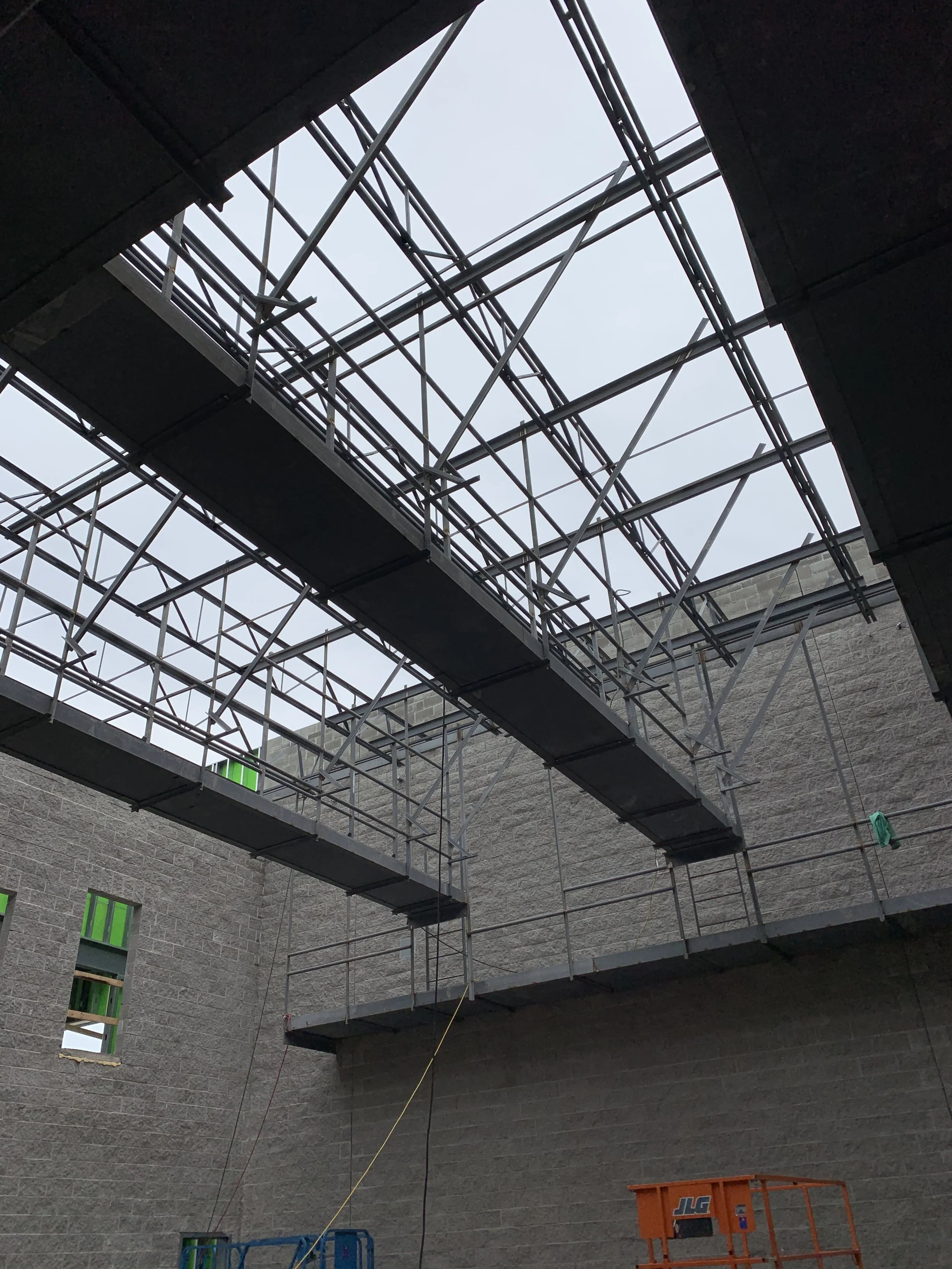 Construction site with scaffolding and metal beams, no roof, and a view of the sky.