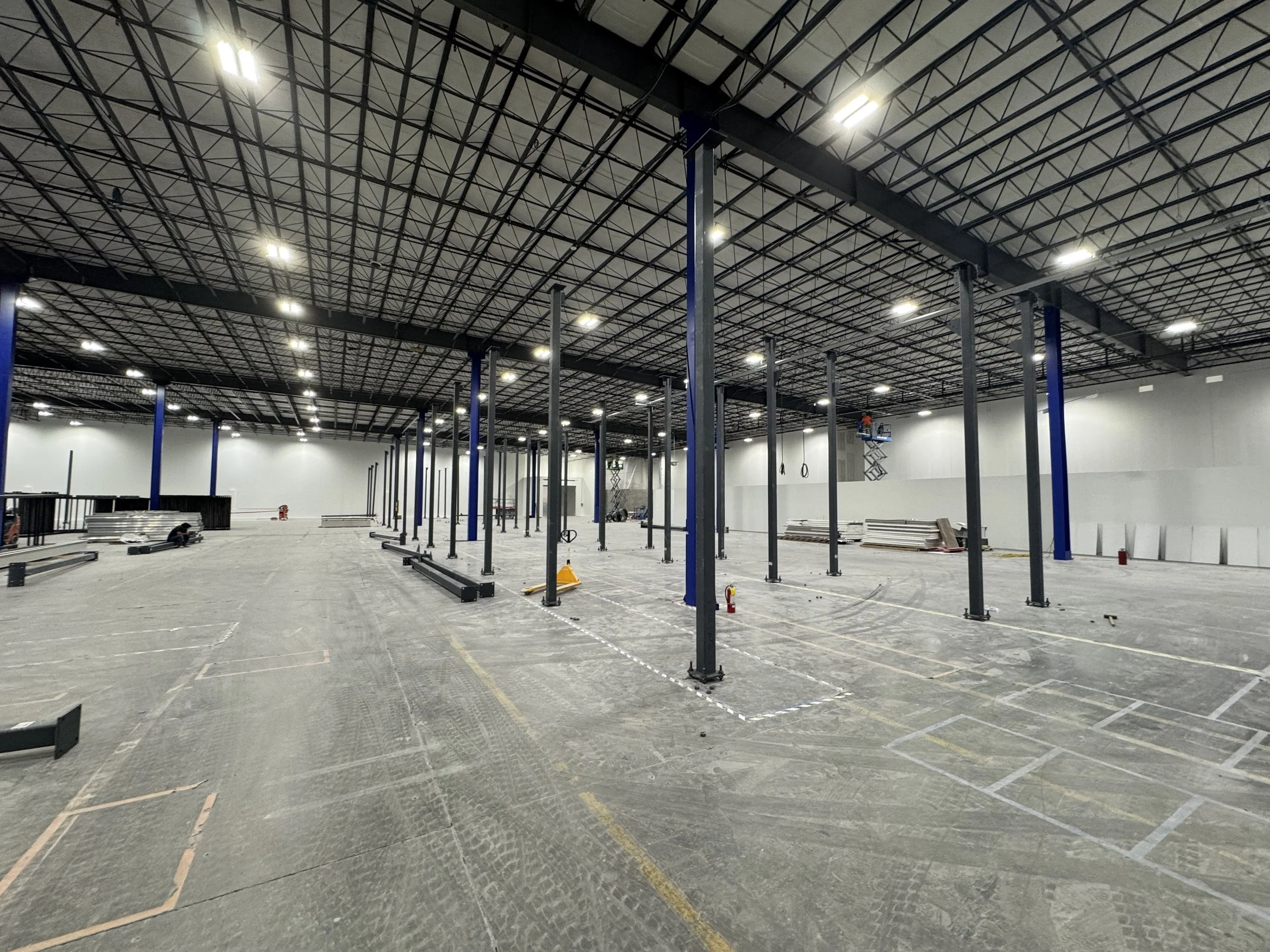 An empty indoor construction site with metal framework for walls and ceiling, and support columns for future structural elements.