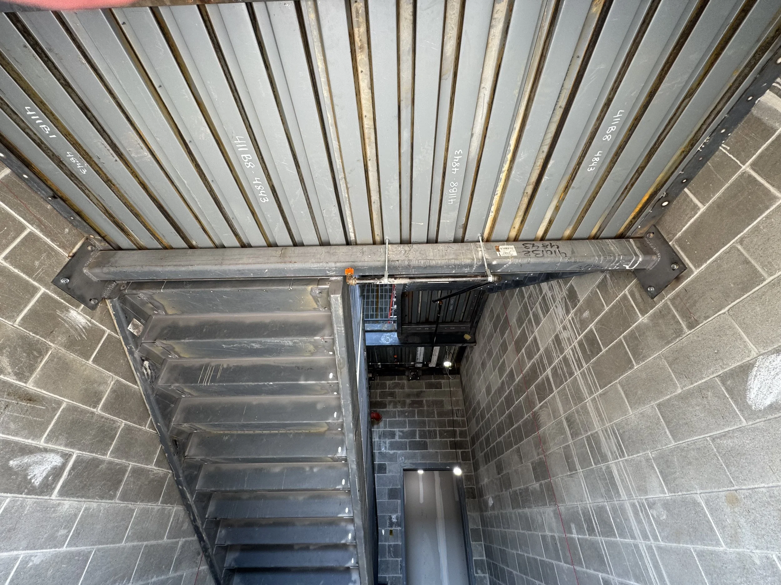 Construction site with metal stairs and a roller shutter door in an industrial building interior with brick walls.