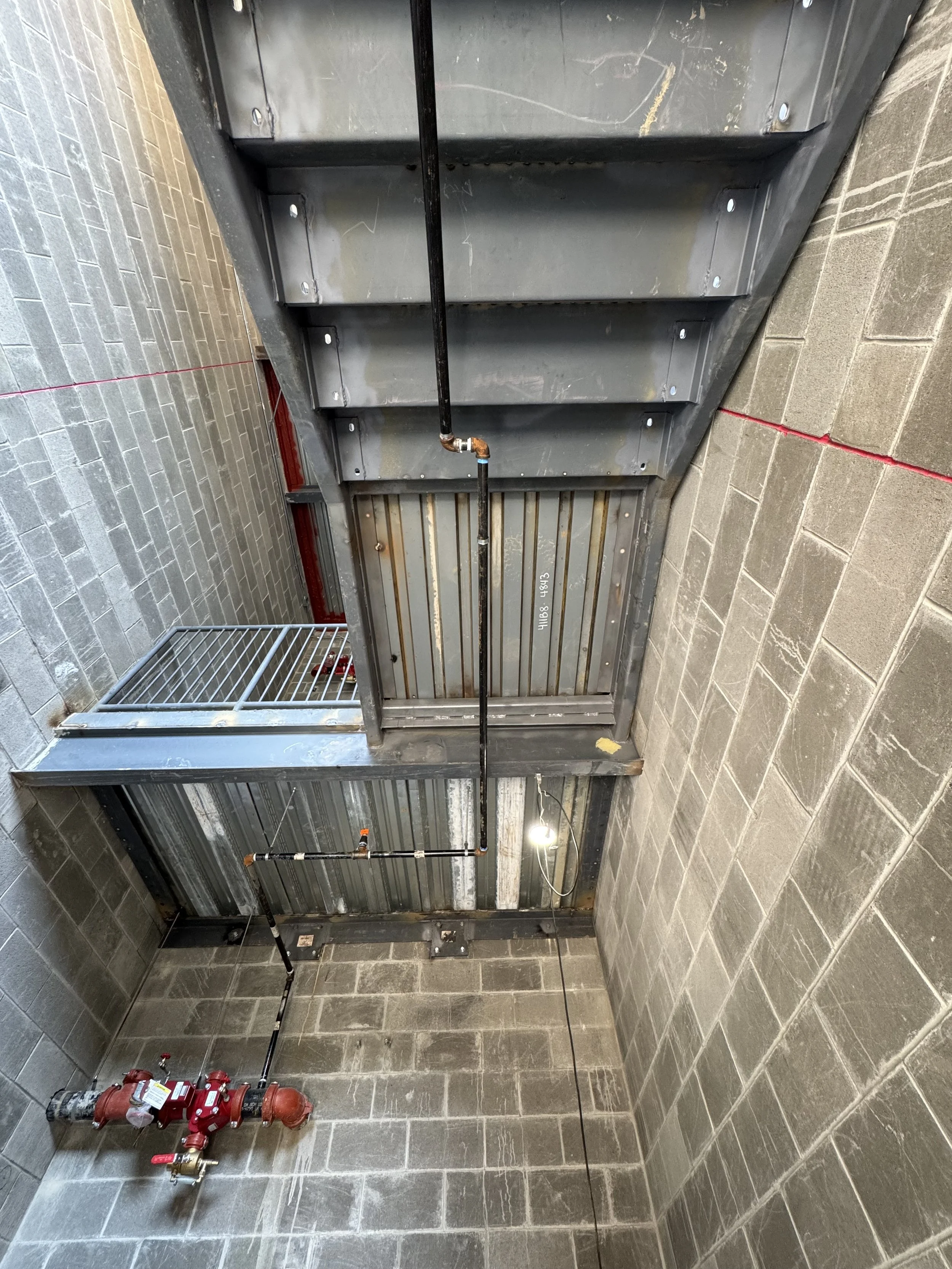 View of an industrial sprinkler system installed on a low ceiling next to a metal staircase and brick walls.