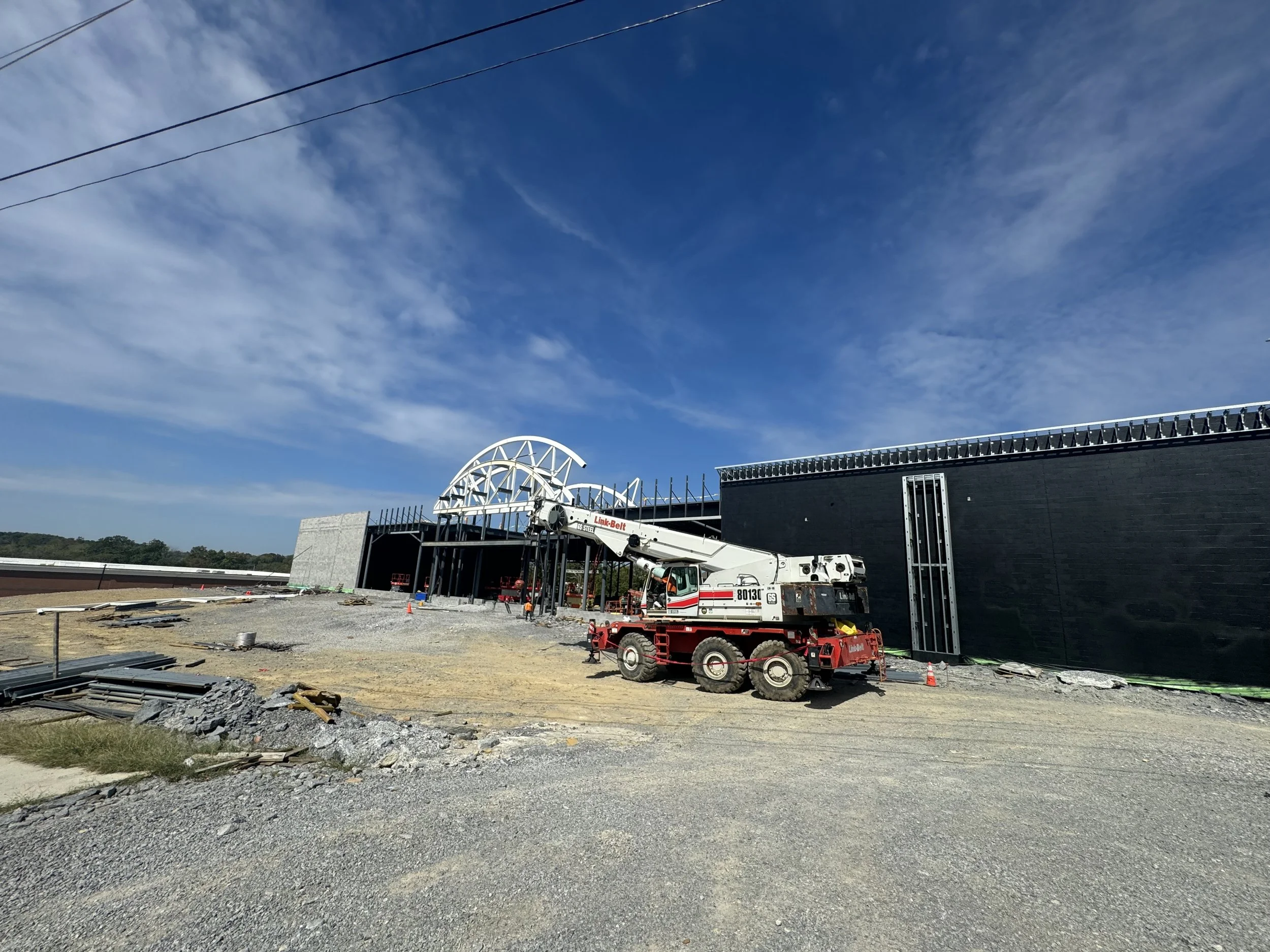 Construction site with large crane in front of a building under construction, partly covered with black material, with a blue sky and wispy clouds overhead.
