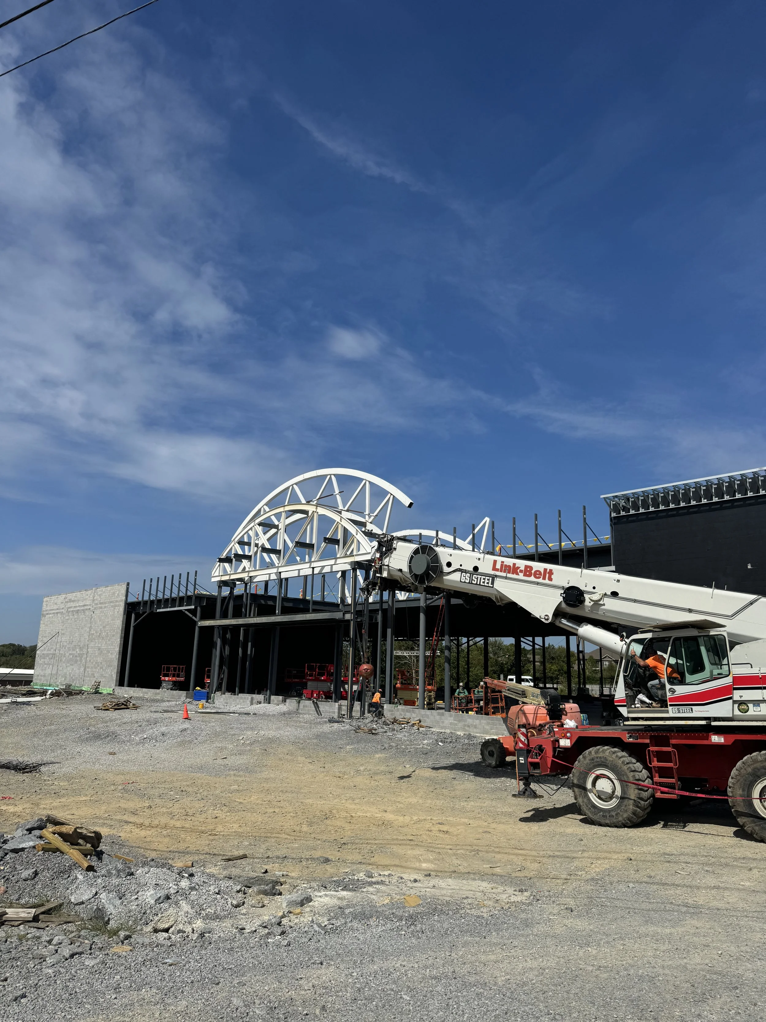 Construction site with a building under construction, a boom lift, and workers present, with a blue sky overhead.
