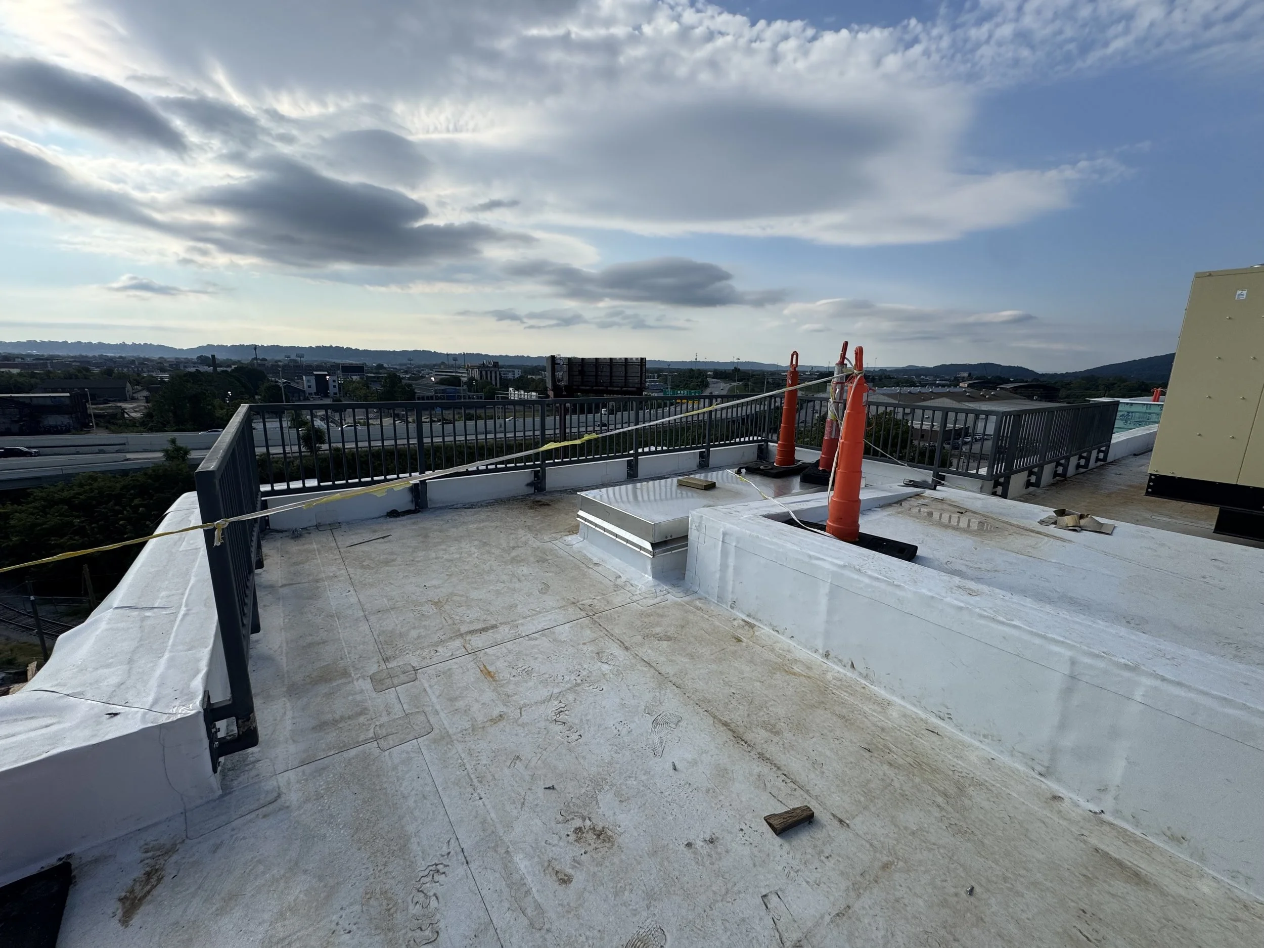 A rooftop with safety guardrails, orange construction cones, and a cloudy sky in the background.