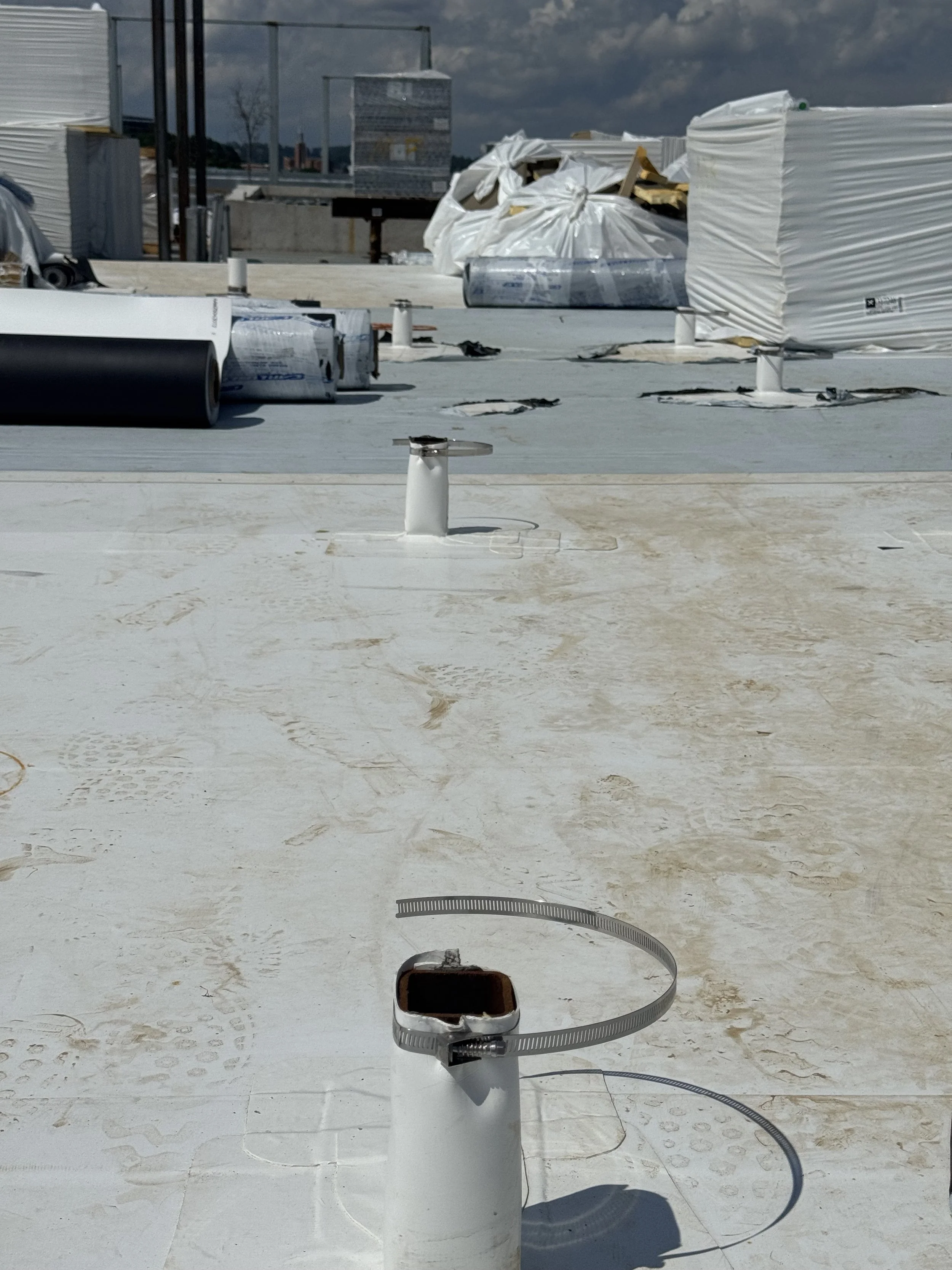 Construction rooftop with various materials, pipes, and equipment, under cloudy sky.