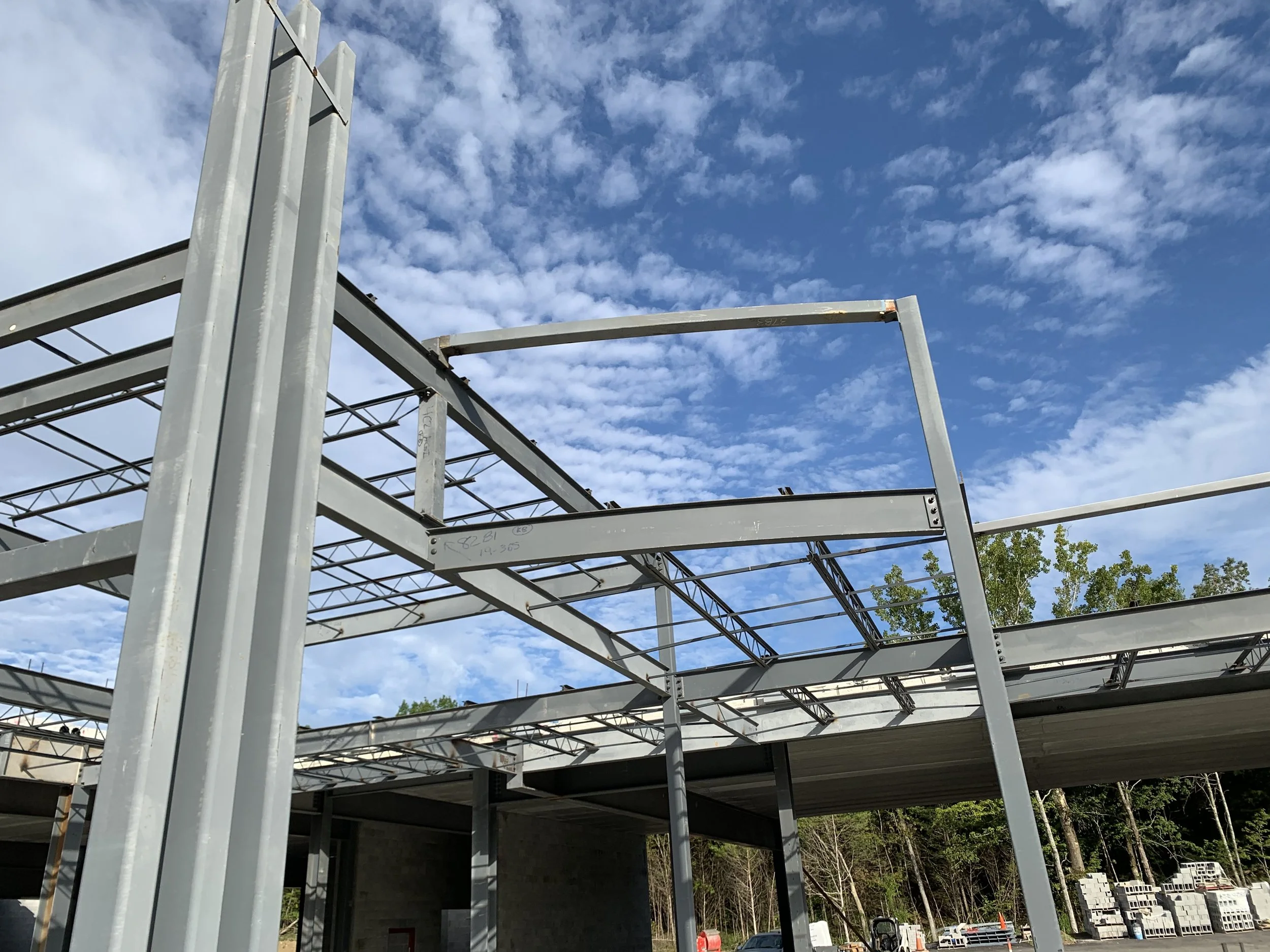 Construction site with metal framework and a blue sky with scattered clouds.