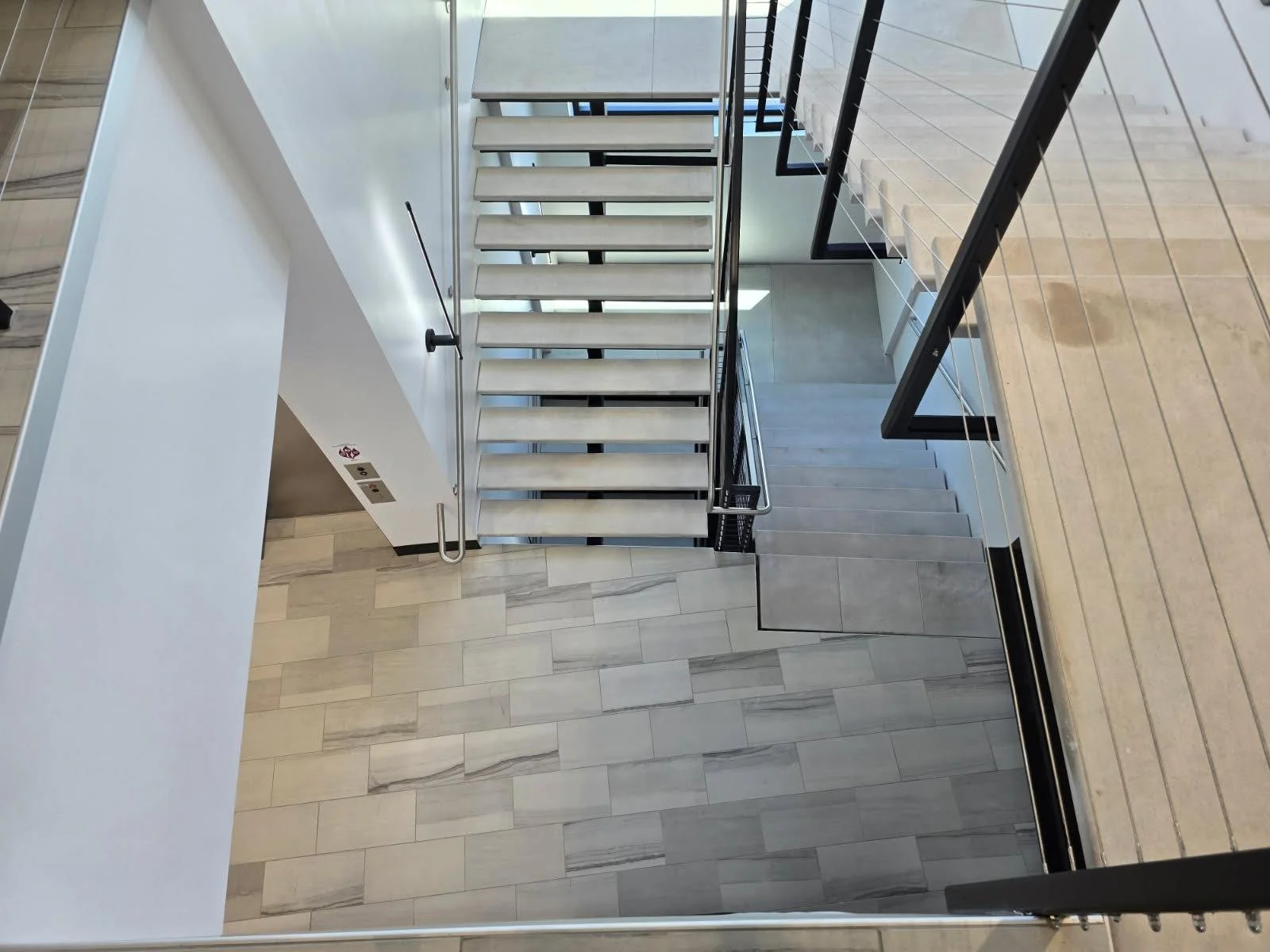 Modern staircase inside a building with white and wooden floors, glass railings, and metal supports.