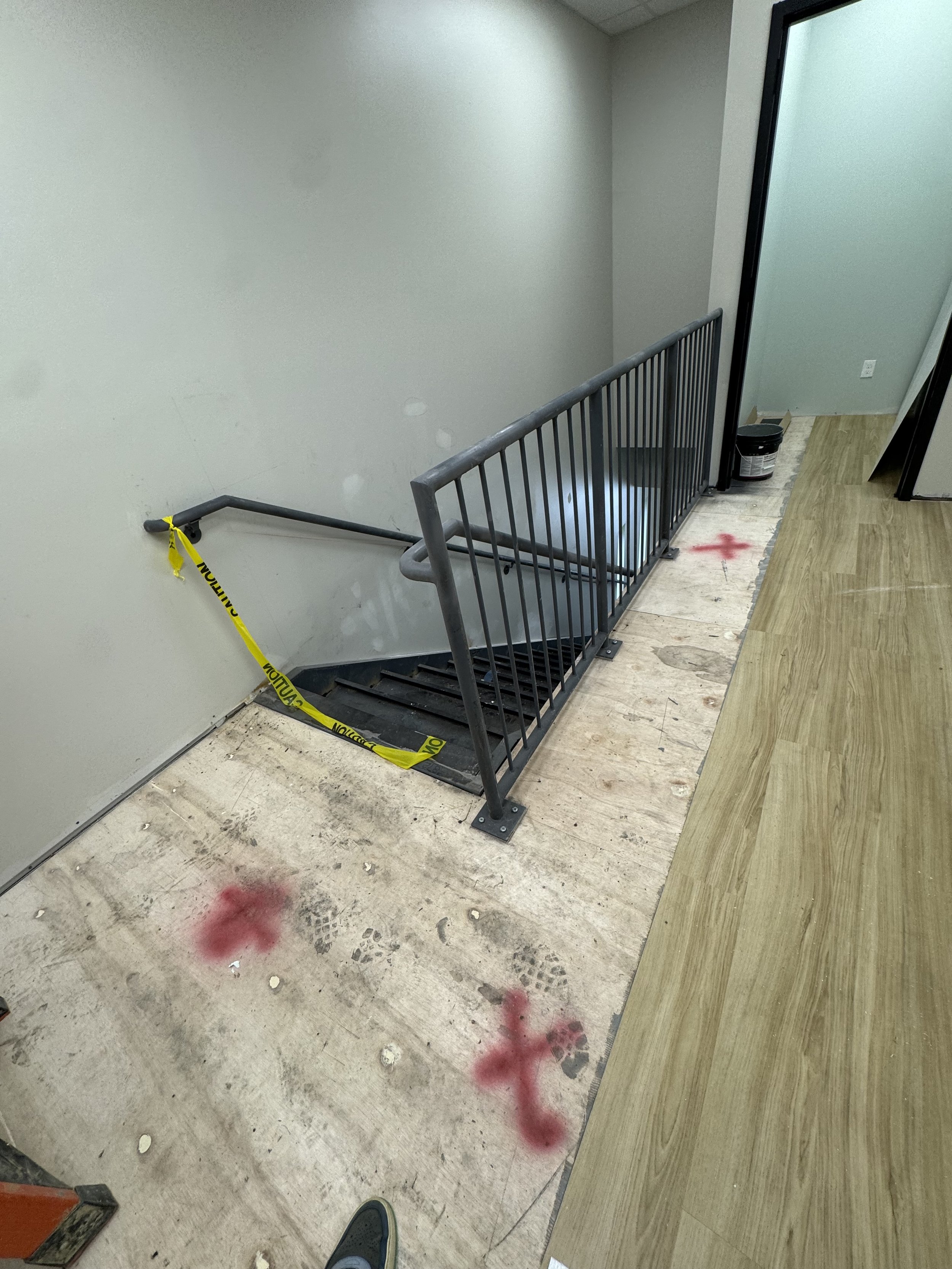Construction site by staircase with caution tape, red spray paint marks, and unfinished flooring.