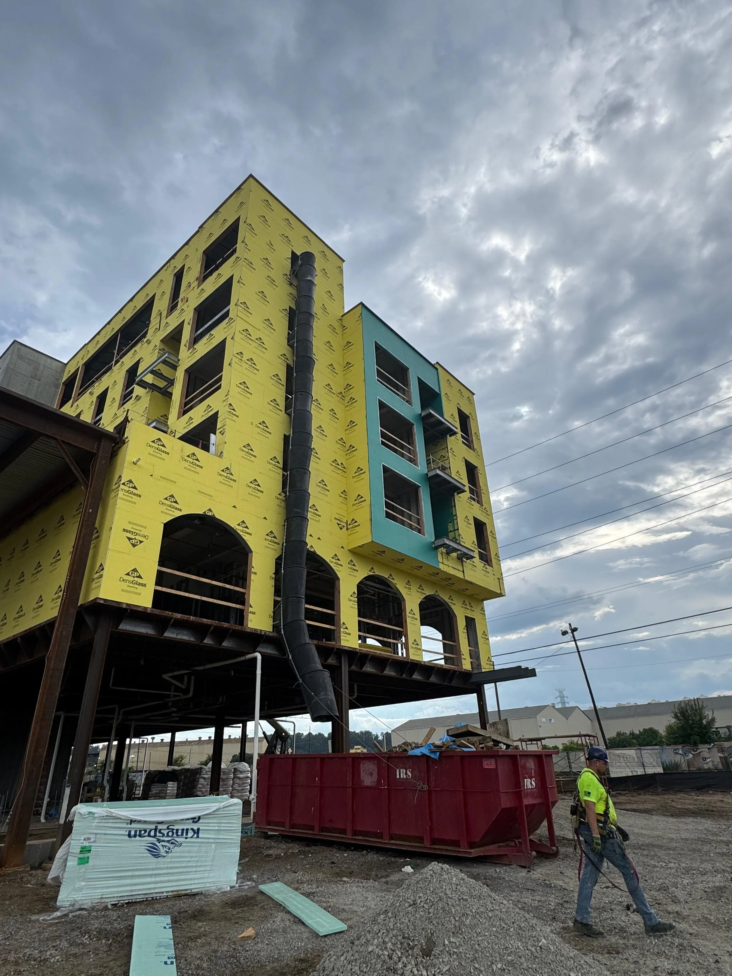 Construction site with a multistory building under construction, yellow insulation panels, and a construction worker walking by.