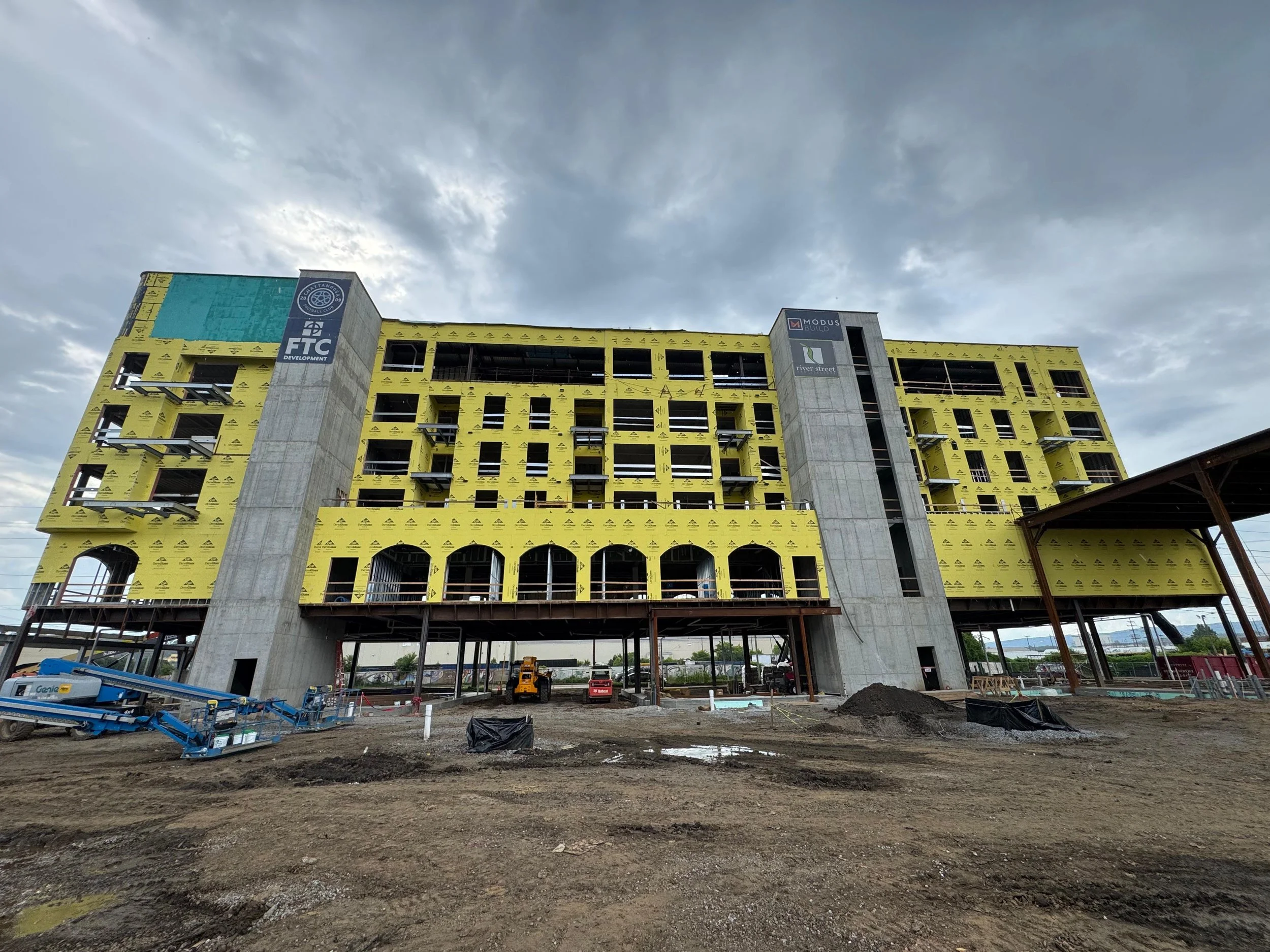 Construction site of a multi-story building with yellow insulation and concrete columns, under cloudy sky.