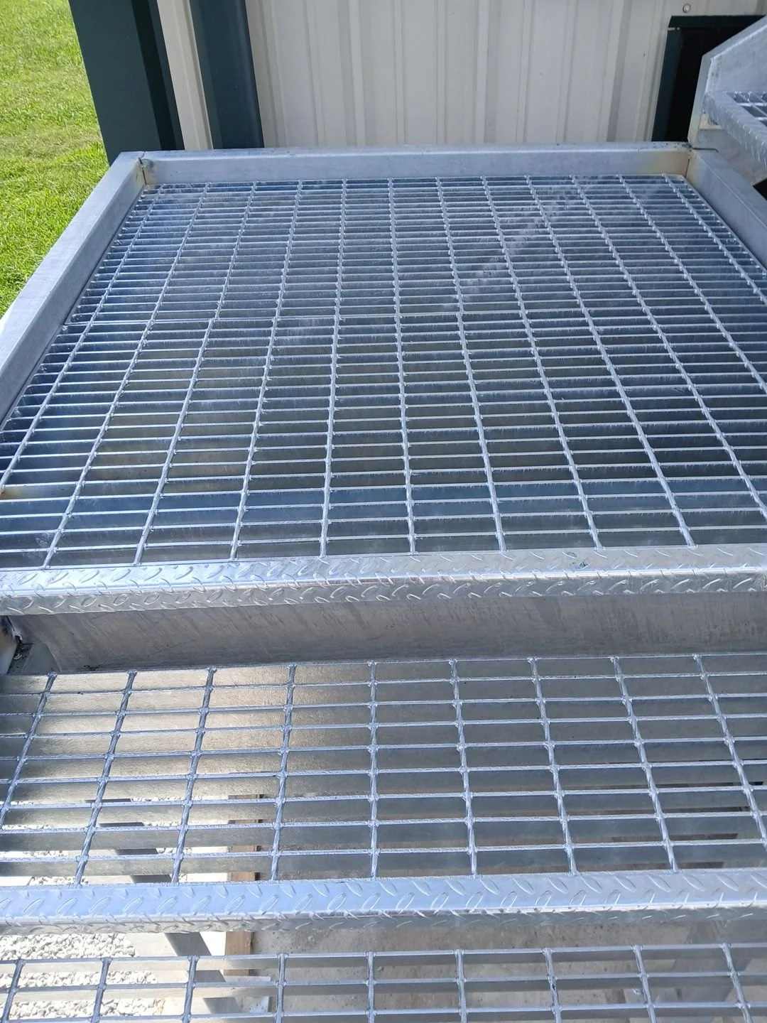 Two metal wire mesh platforms outdoors next to a building with beige siding and a green door.