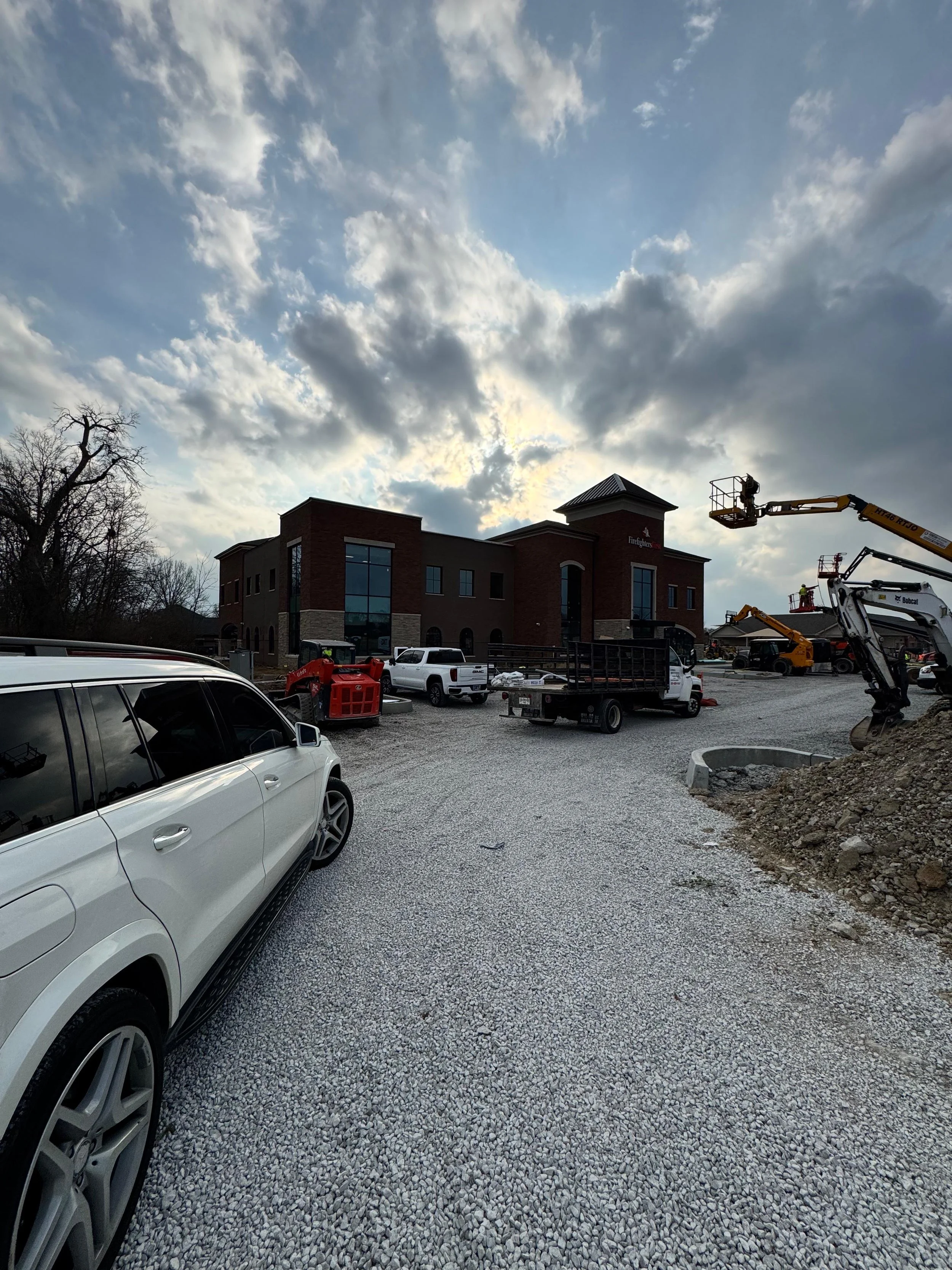 Construction site with vehicles and equipment around a building under construction, cloudy sky in the background.