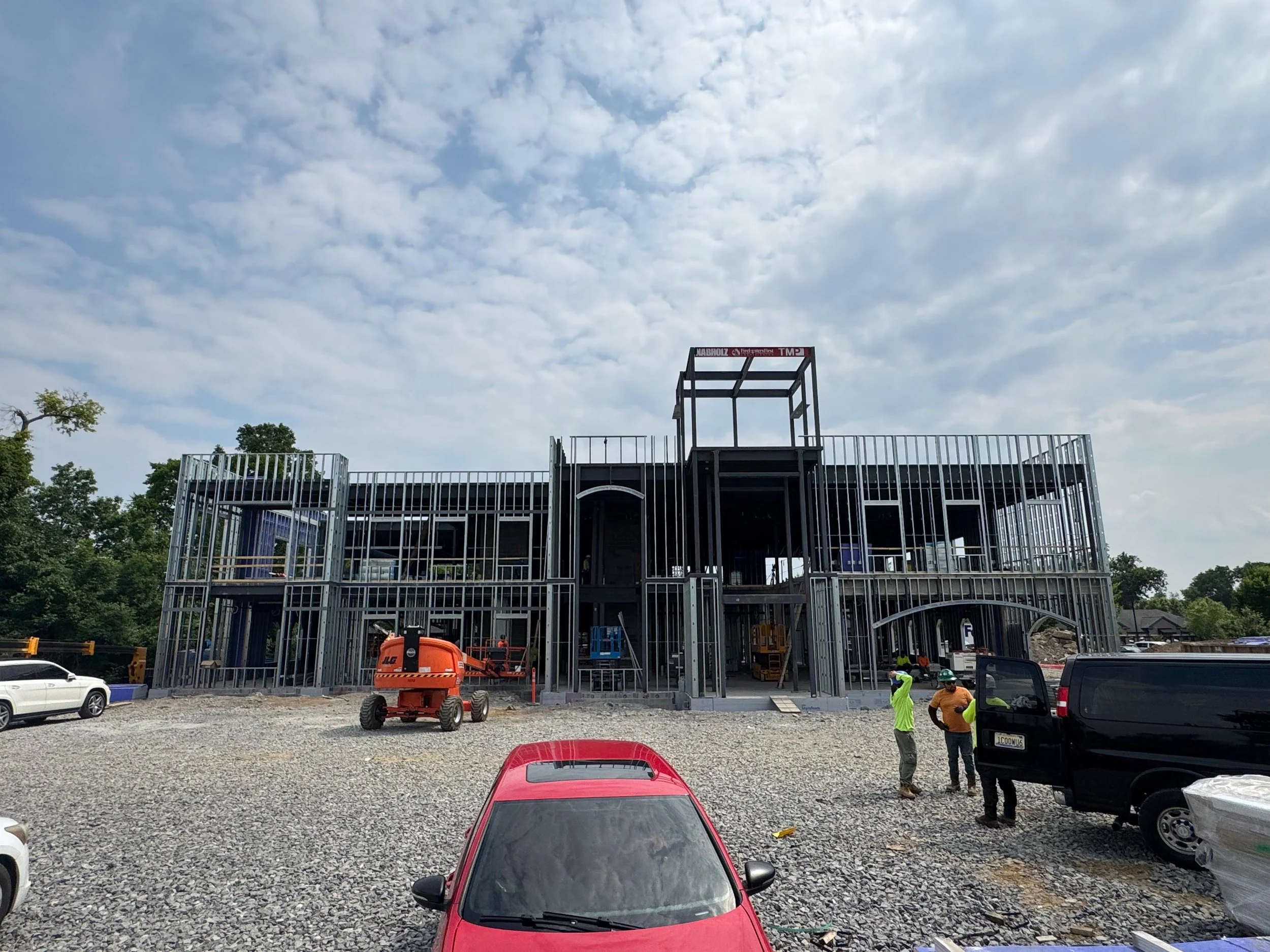 Construction site with a building frame made of steel beams and scaffolding, several construction workers and vehicles present.