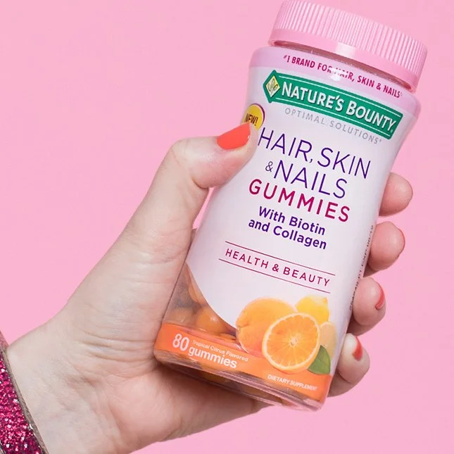 Hand holding a vitamin bottle on a pink background