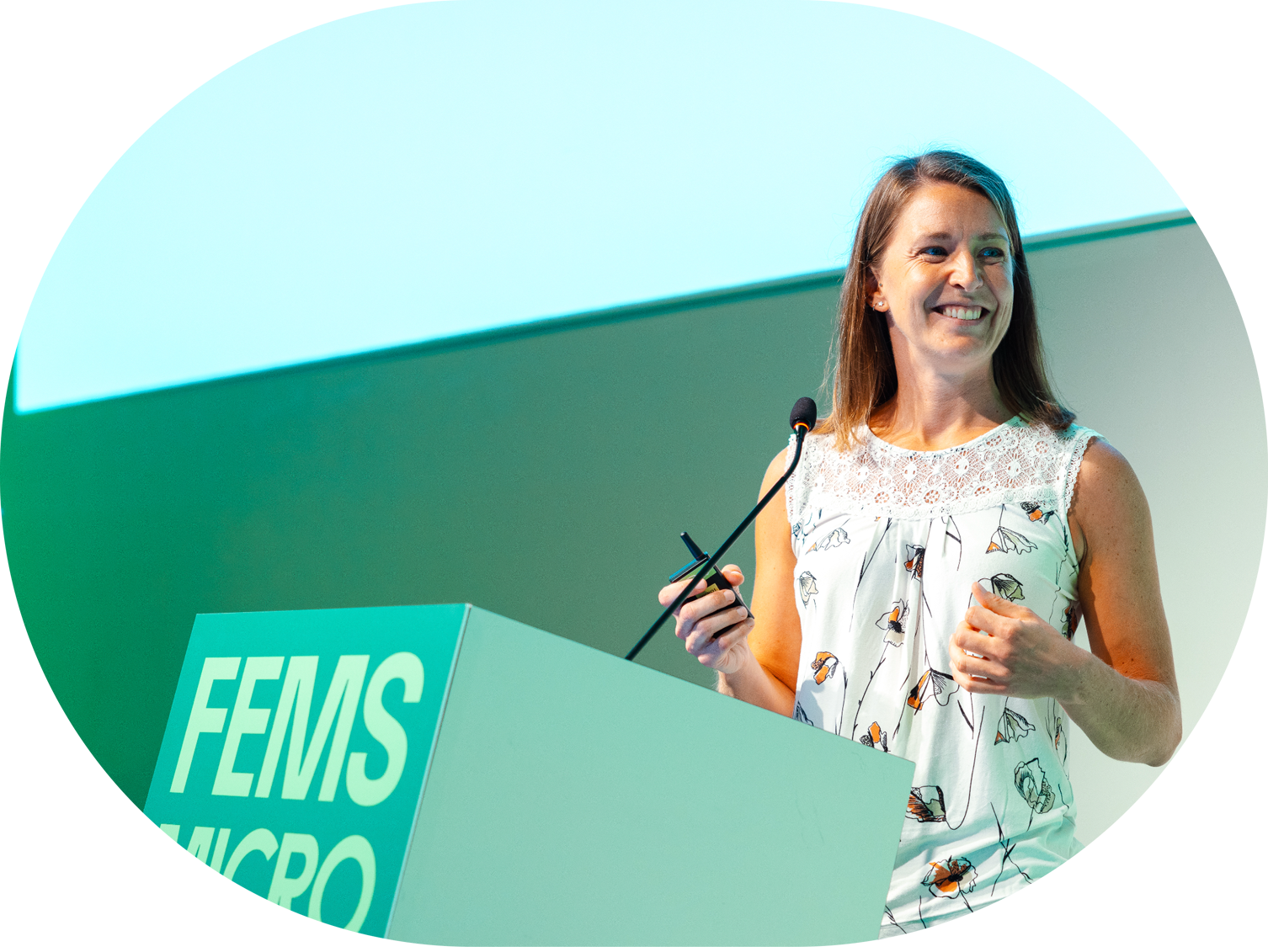 A woman smiling as she speaks at a podium with a banner that reads 'FEMS MICRO'.
