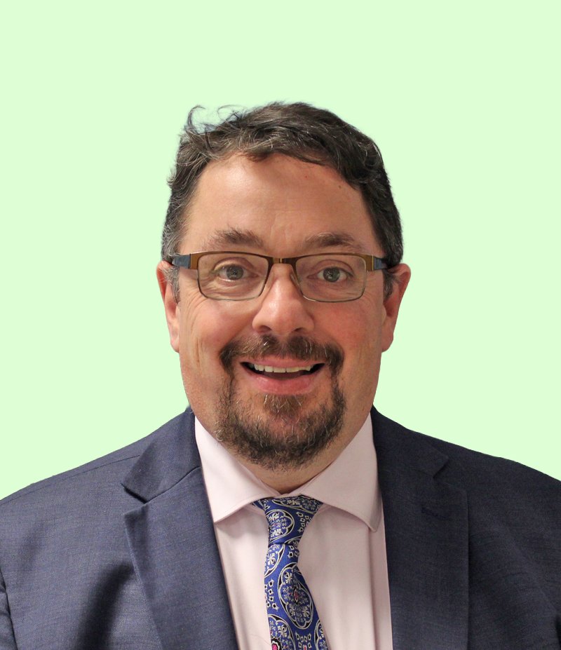 Man with glasses wearing a suit and tie, smiling, against a light green background.