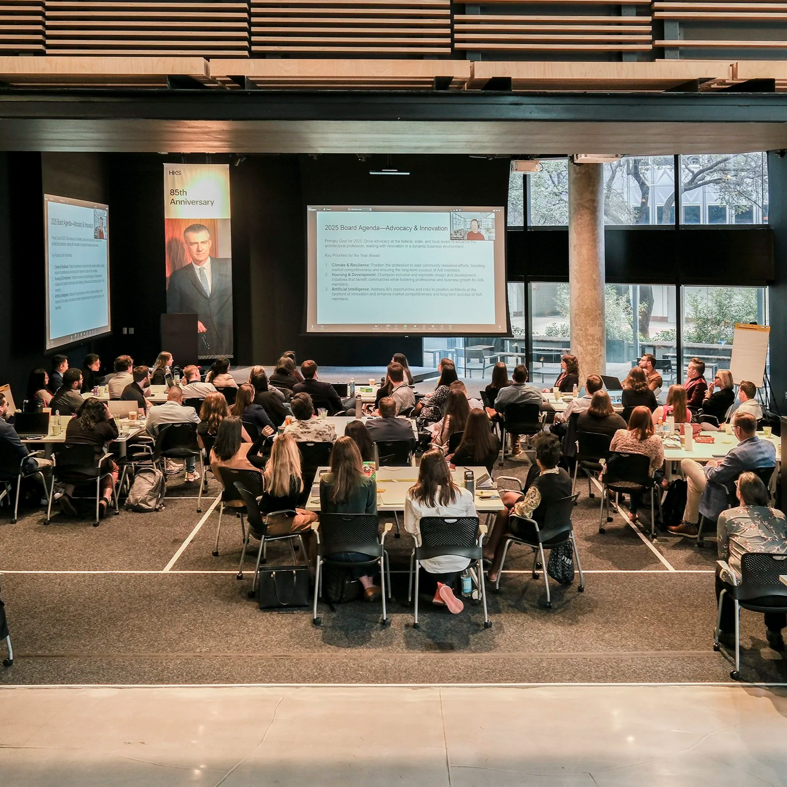 A group of people in a large conference room listens to a presentation by 2025 AIA President Evelyn Lee, FAIA