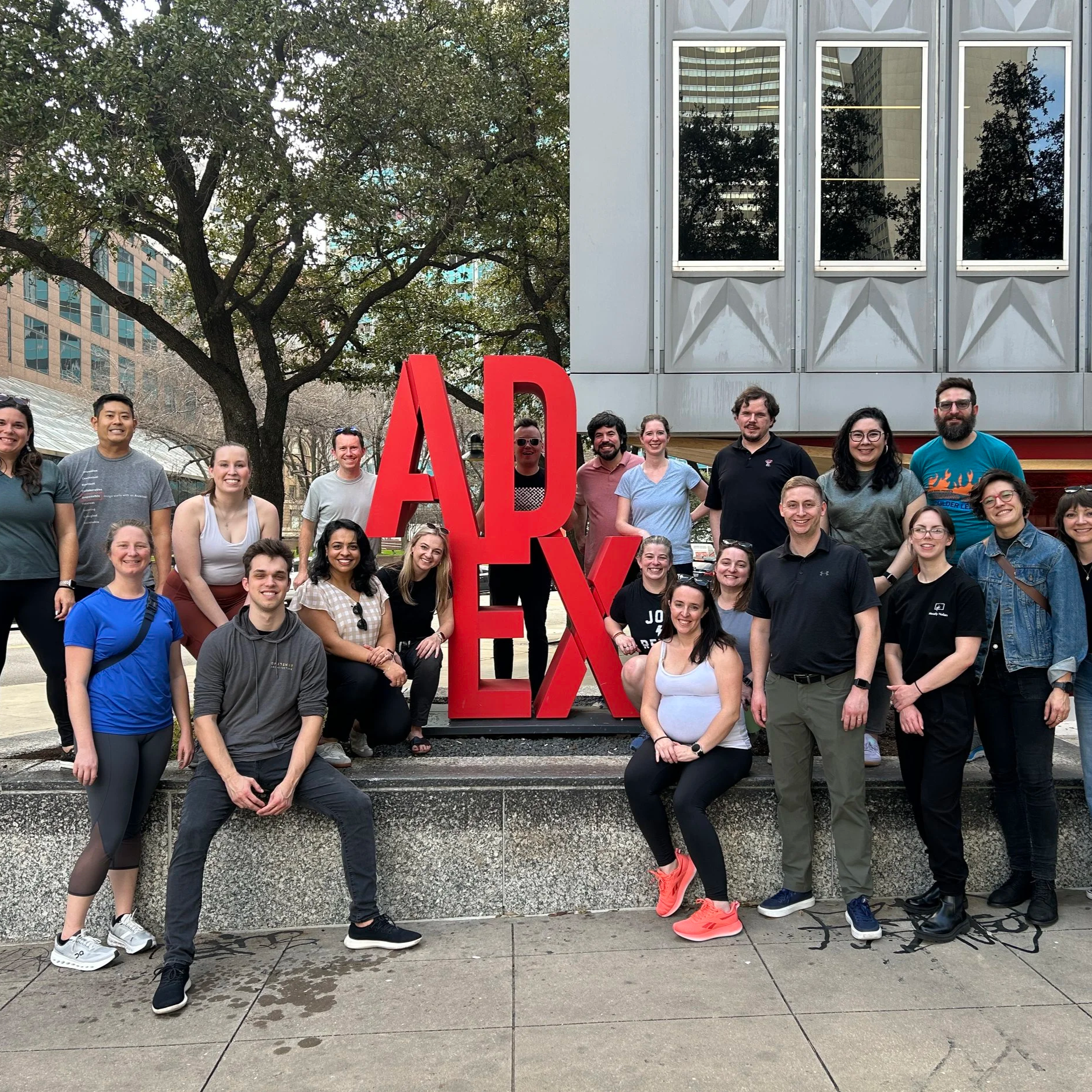 A group of people gathers outdoors around a sign that says ADEX