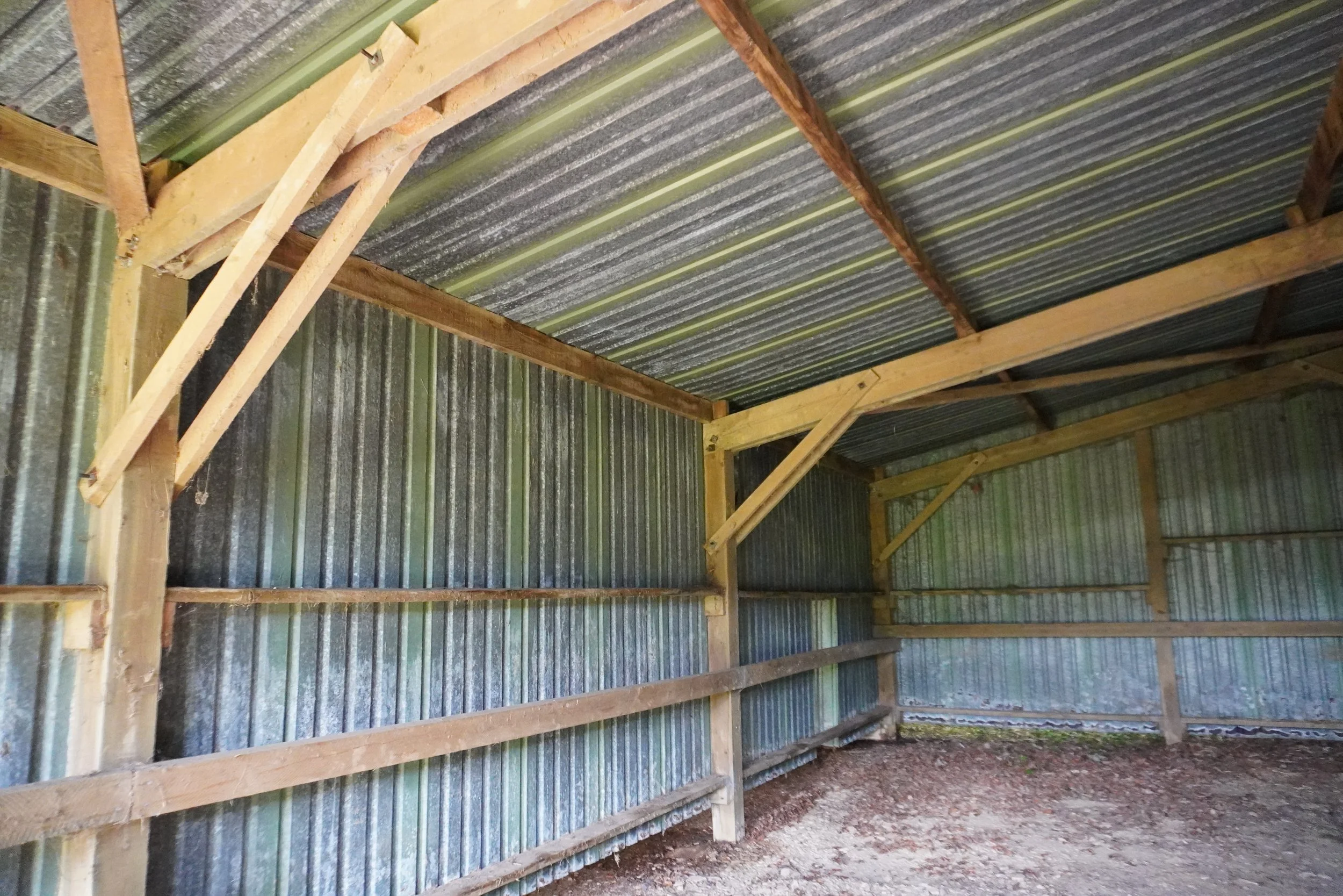 Interior of a small wooden shed or barn with corrugated metal walls and roof, featuring exposed wooden framing and a dirt floor.