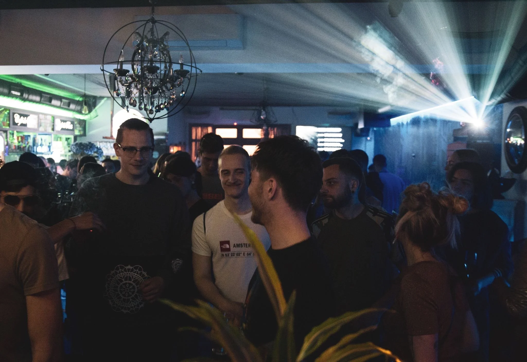 People socializing in a nightclub with colorful lights and a chandelier hanging from the ceiling.