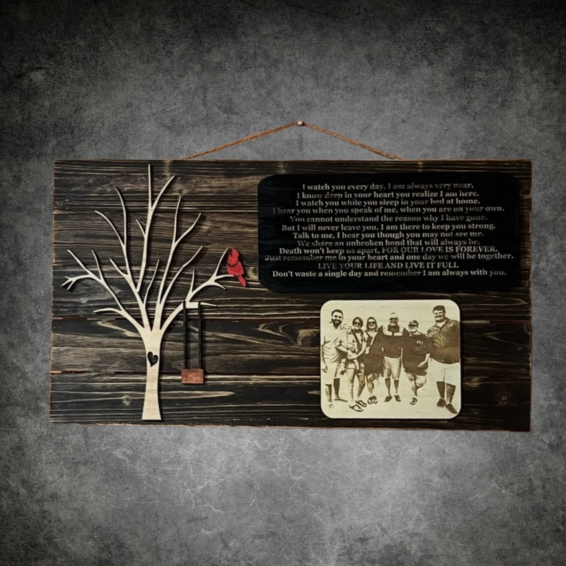 Decorative wall hanging with a tree silhouette, a red bird, a swing, a black plaque with a poem, and a photo of a group of people.