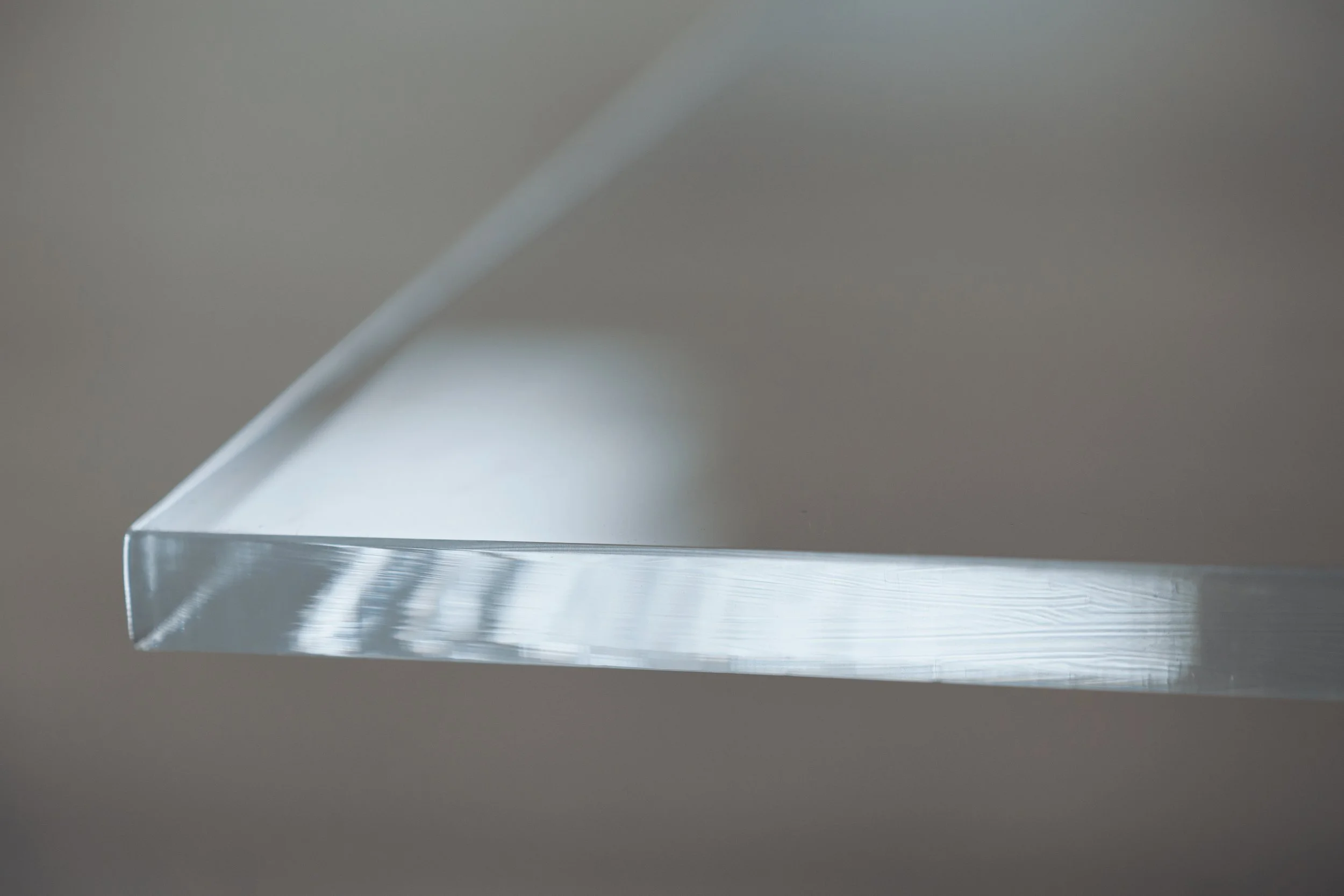 Close-up of a transparent, rectangular glass or acrylic object with a bevelled edge, reflecting light and showing internal patterns or textures.