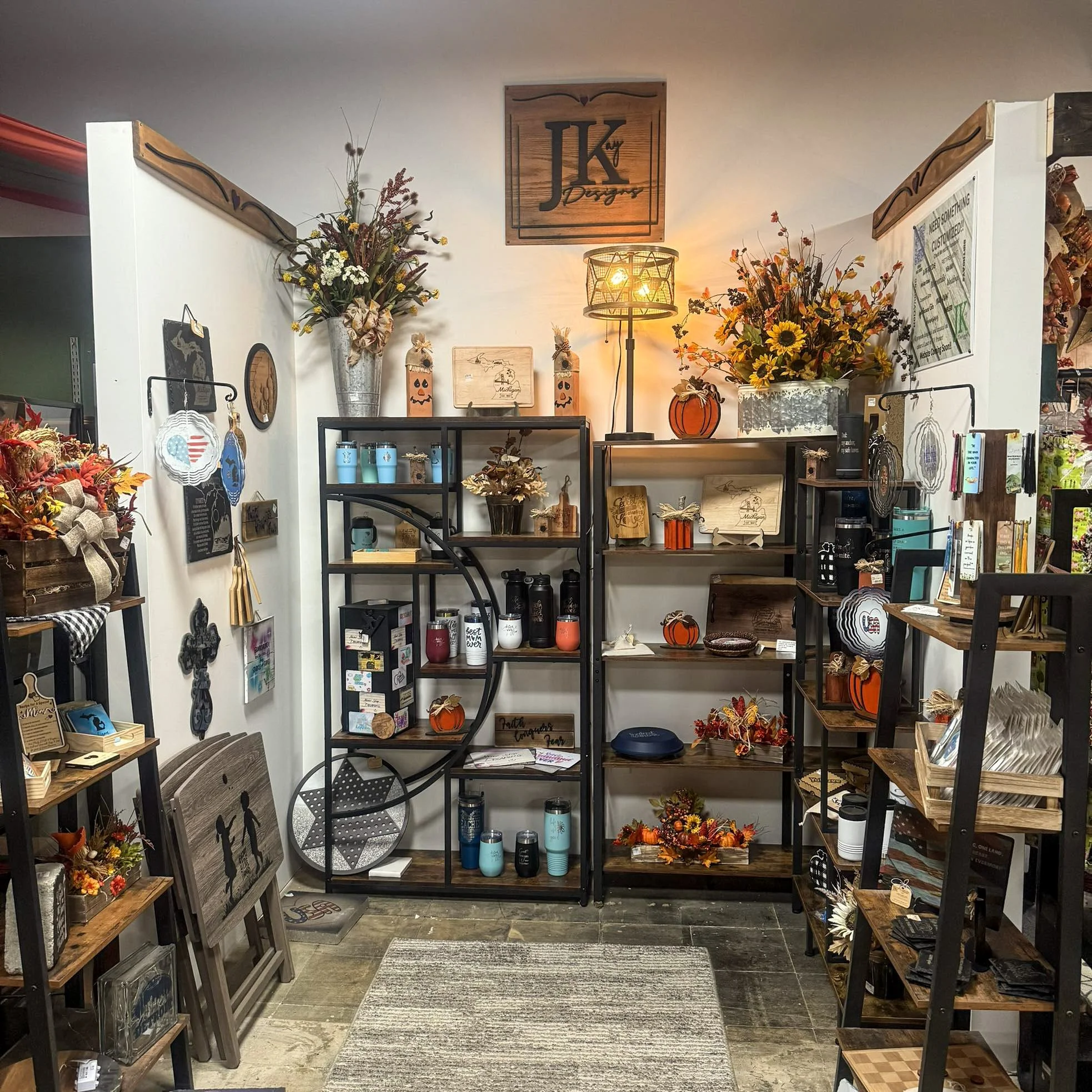 Display of fall-themed home decor and accessories on shelves, including artificial flowers, pumpkins, candles, and wooden signs in a boutique store.