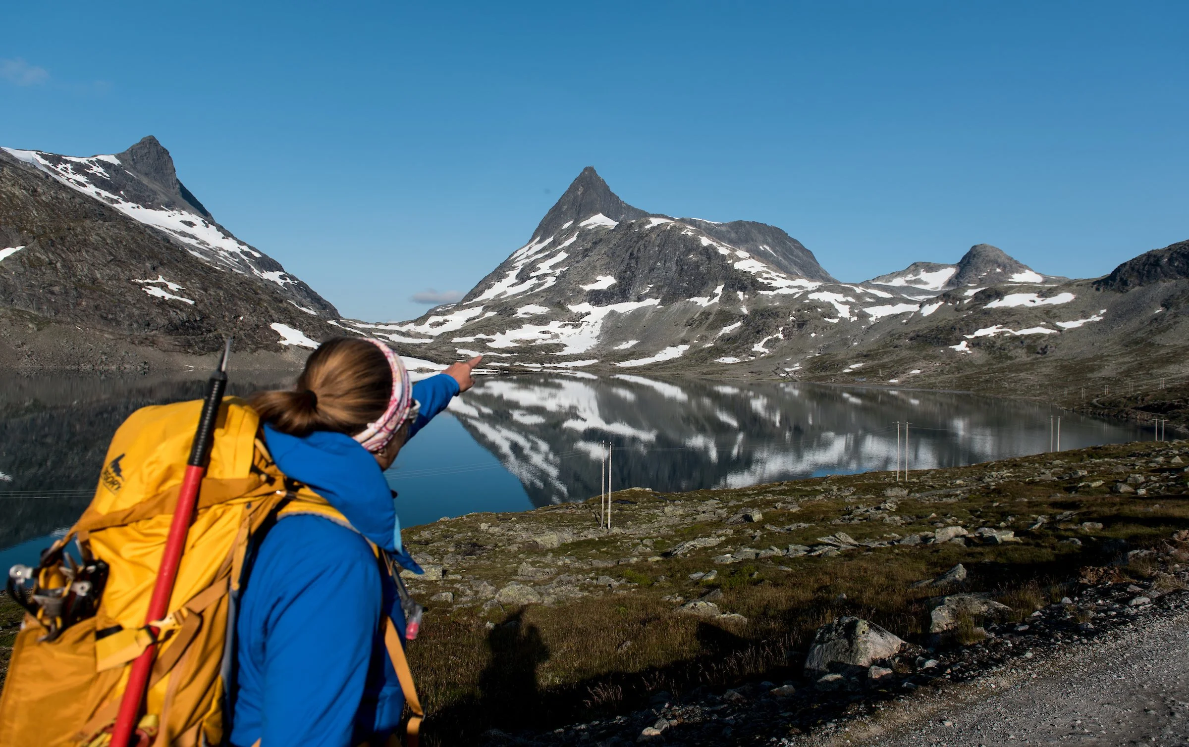 Seks personer på ski opp en snøtopp med snødekte fjell i bakgrunnen.