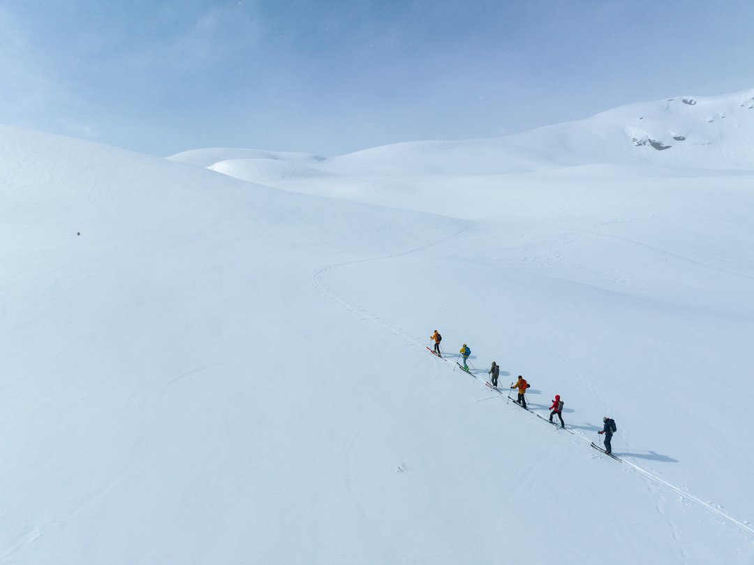 Syvkledde personer på ski i snødekt fjell landskap under en blå himmel.