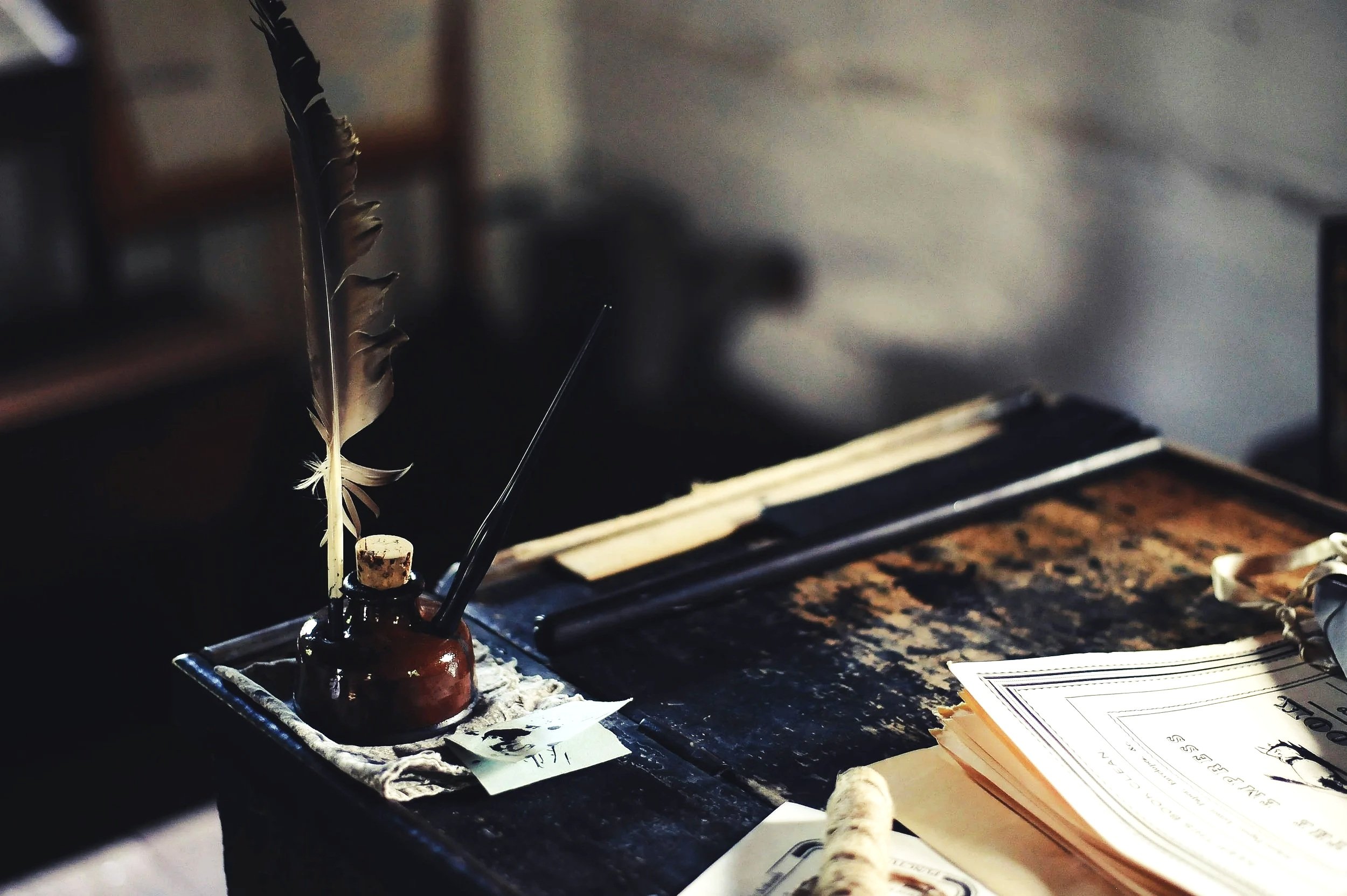 A vintage wooden desk with an ink bottle holding a quill, an open book, and scattered papers.