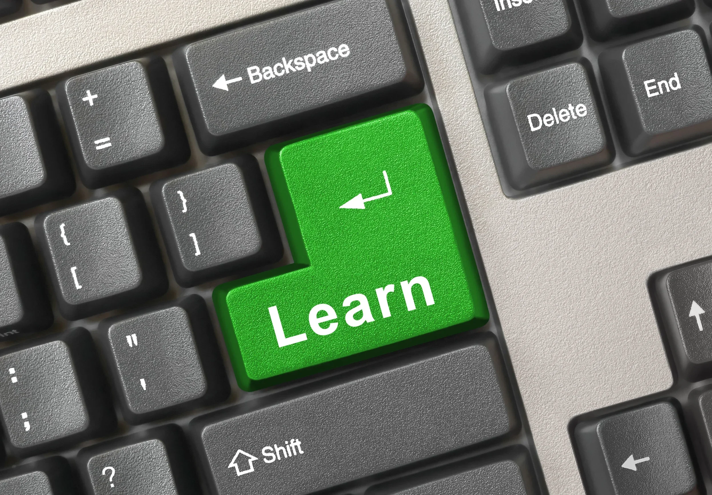 Close-up of a computer keyboard with a green key labeled 'Learn' in white text, surrounded by standard gray keys including Backspace and Delete.