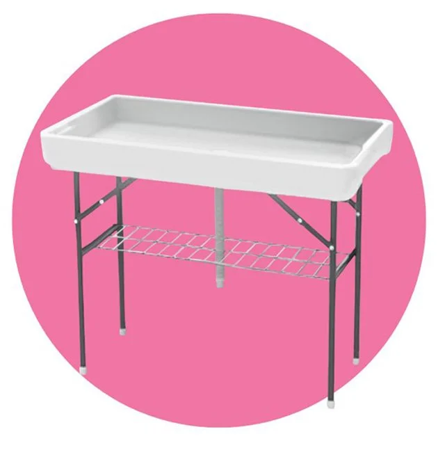 A white cooler table for displaying beverages and ice that is easy to drain with black metal legs and a wire shelf underneath, against a pink circular background.