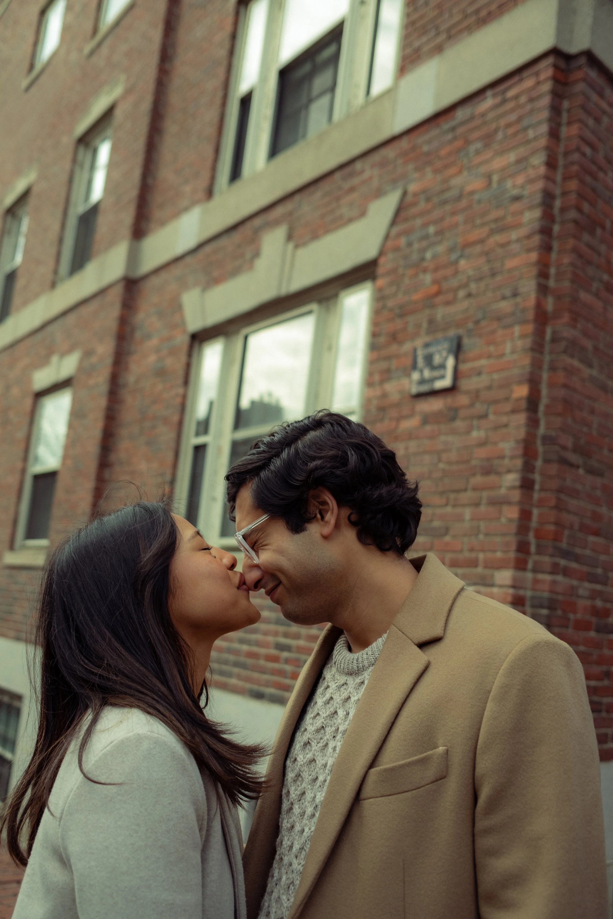 A couple sitting on steps outside a building, looking at each other and smiling. The woman is in a cream dress and the man is in a beige suit.