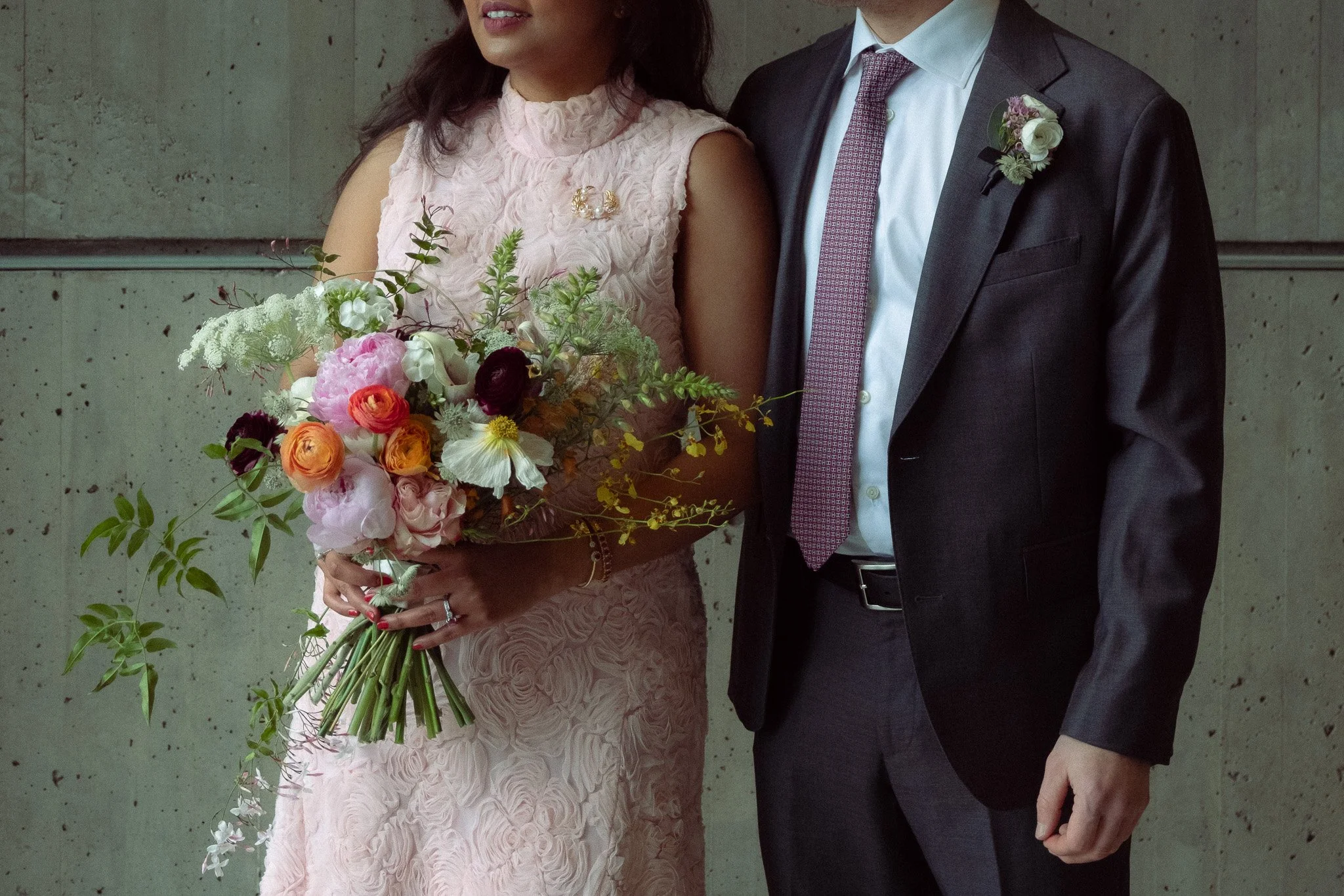 A man and a woman holding hands during an evening outside on a city sidewalk, with the man wearing a light-colored suit and the woman wearing a ring on her finger.
