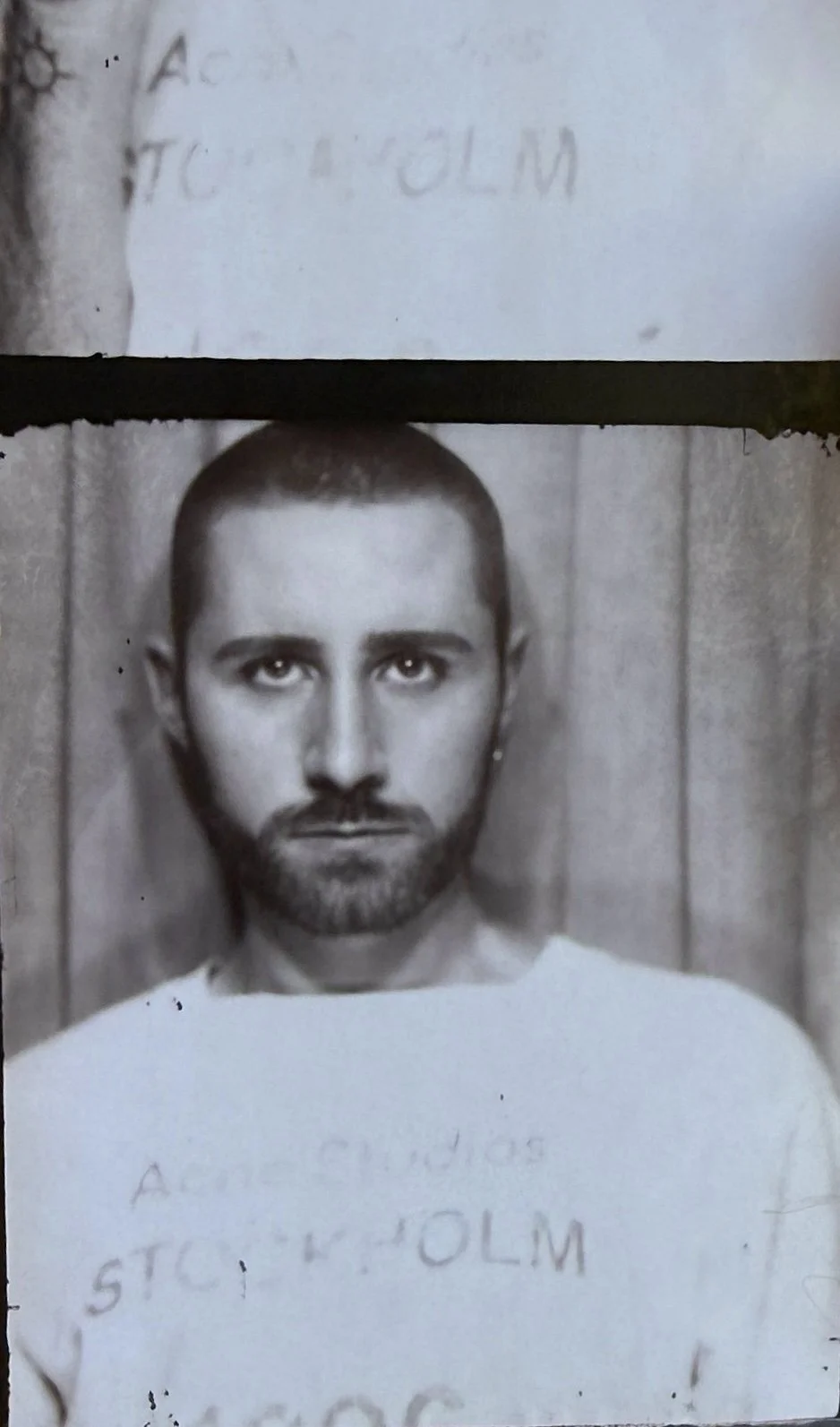 Black and white mugshot of a man with short hair and a beard, against a wooden background.