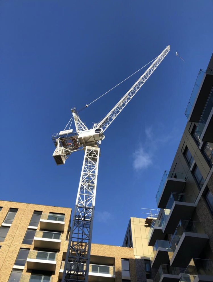 A tall white construction crane towers over modern apartment buildings under a clear blue sky.