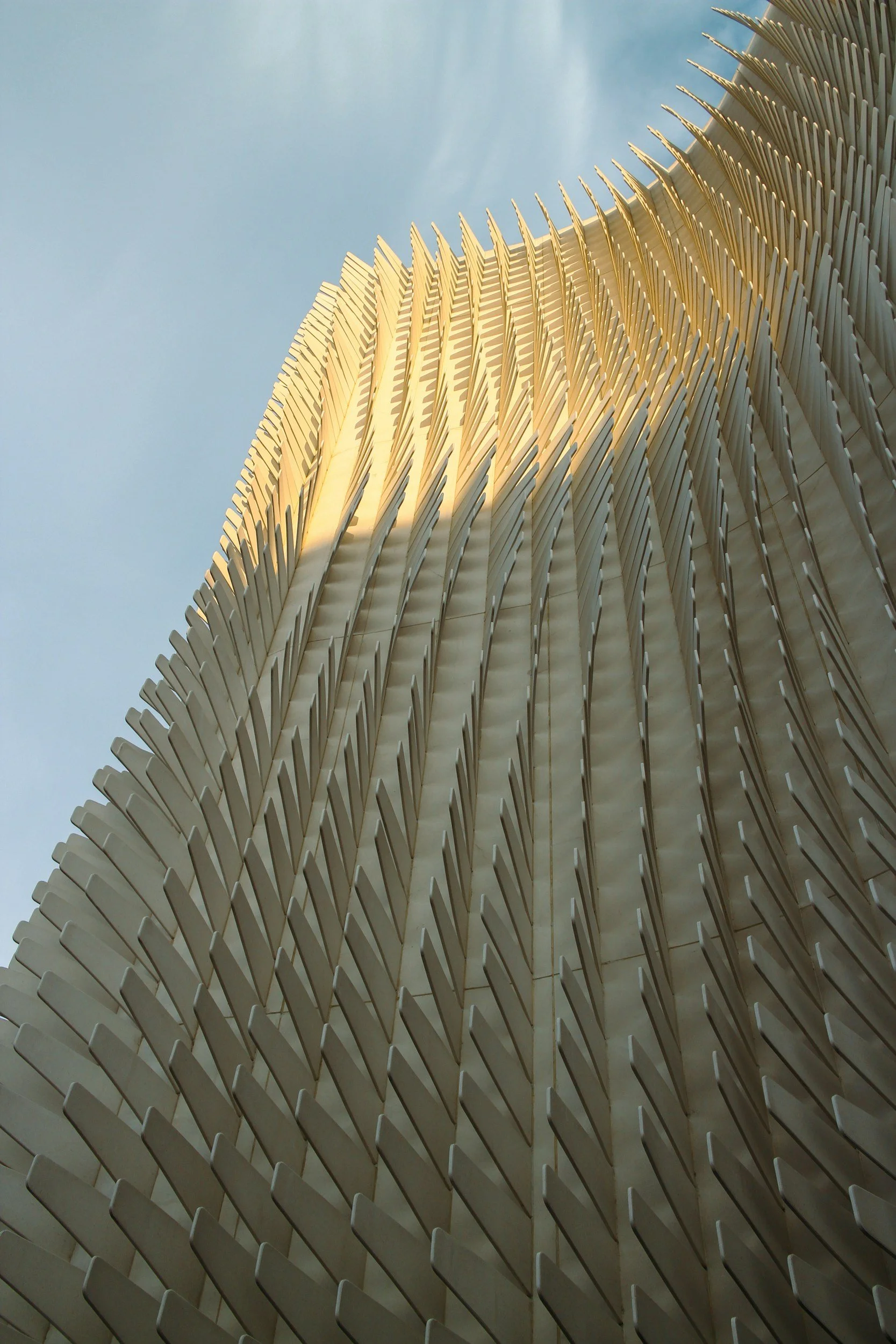 Close-up view of a modern architectural building with a curved facade covered in evenly spaced white vertical fins, set against a clear blue sky.