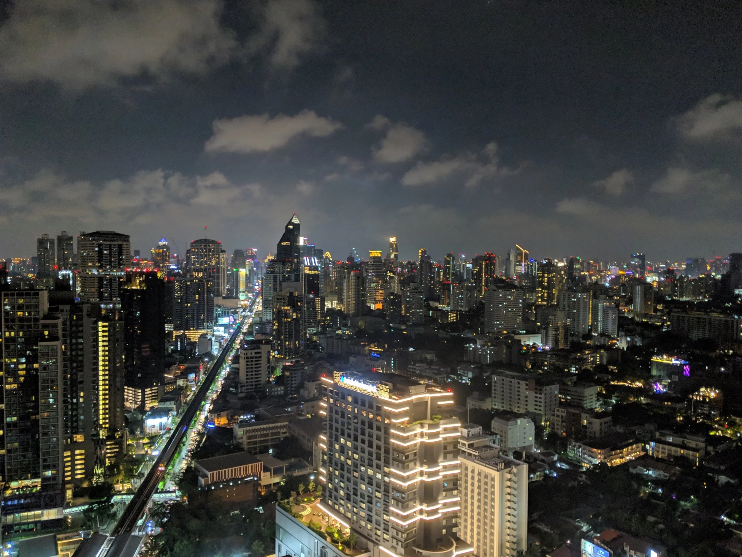 Nighttime city skyline of a large urban area with high-rise buildings, illuminated streets, and clouds overhead.