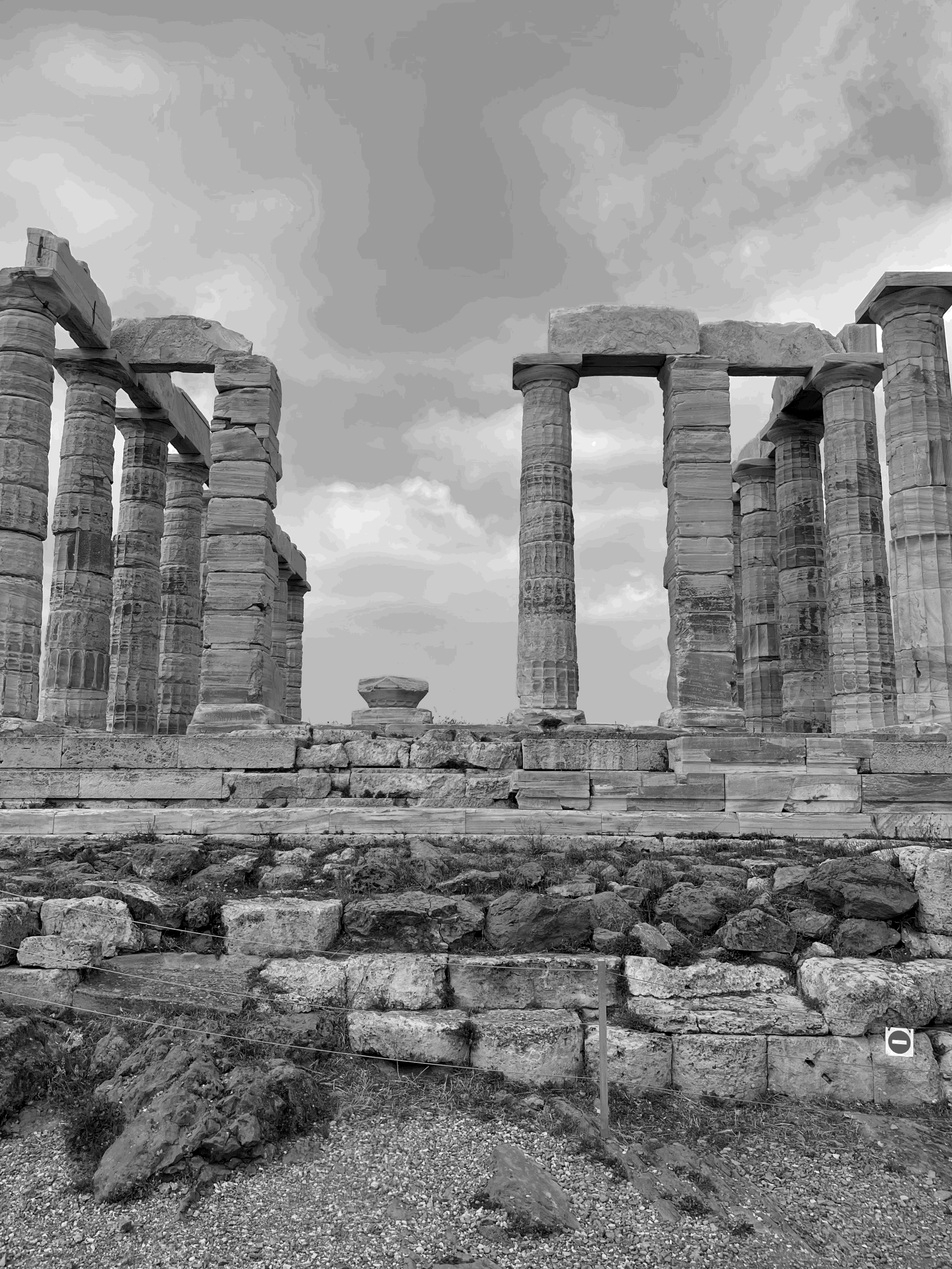 Ancient Greek ruins with tall stone columns on a cloudy sky background.