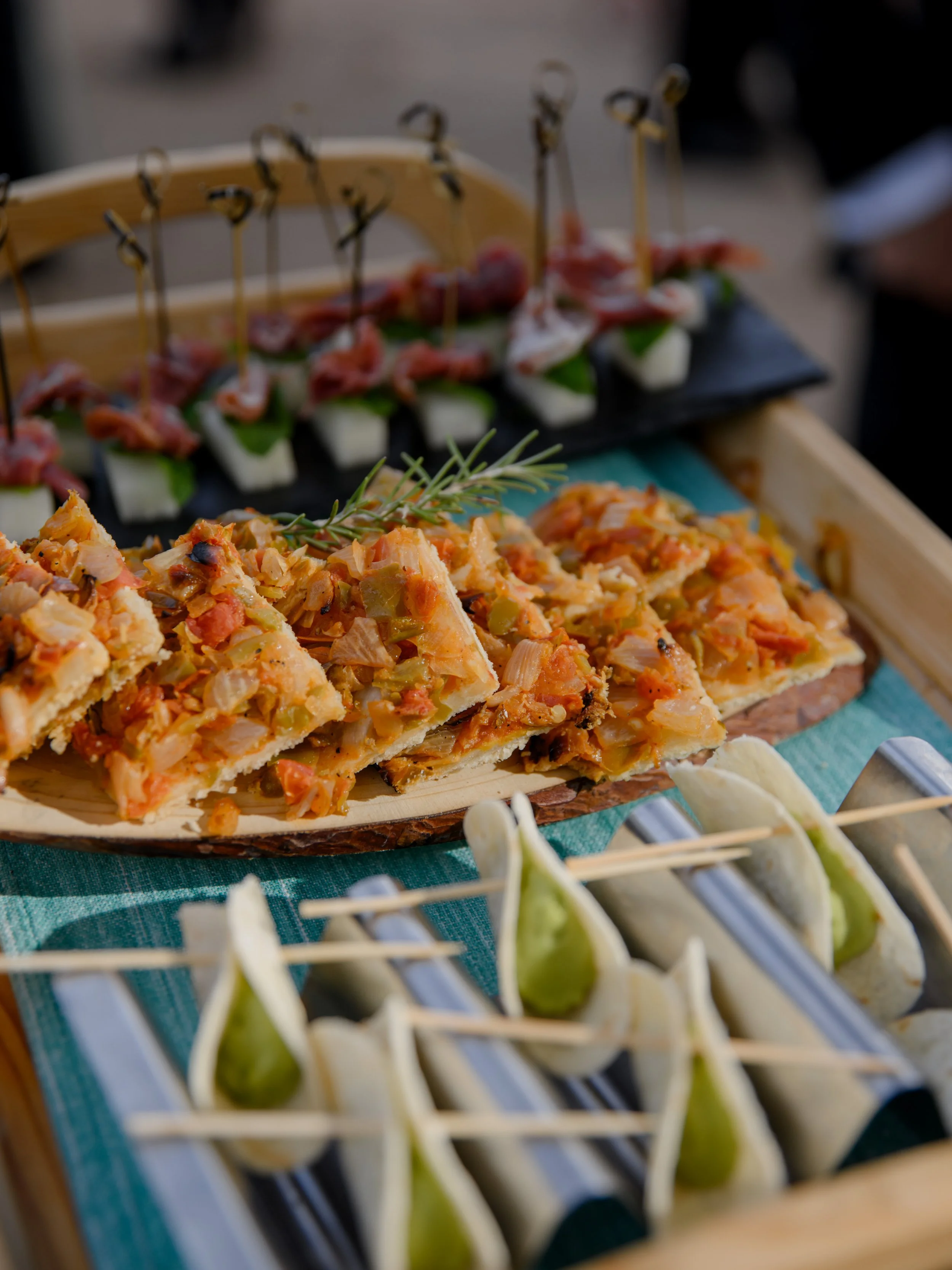 Assorted appetizers including small sandwiches with green filling and skewers with cheese, cucumber, and meat, presented on a tray.