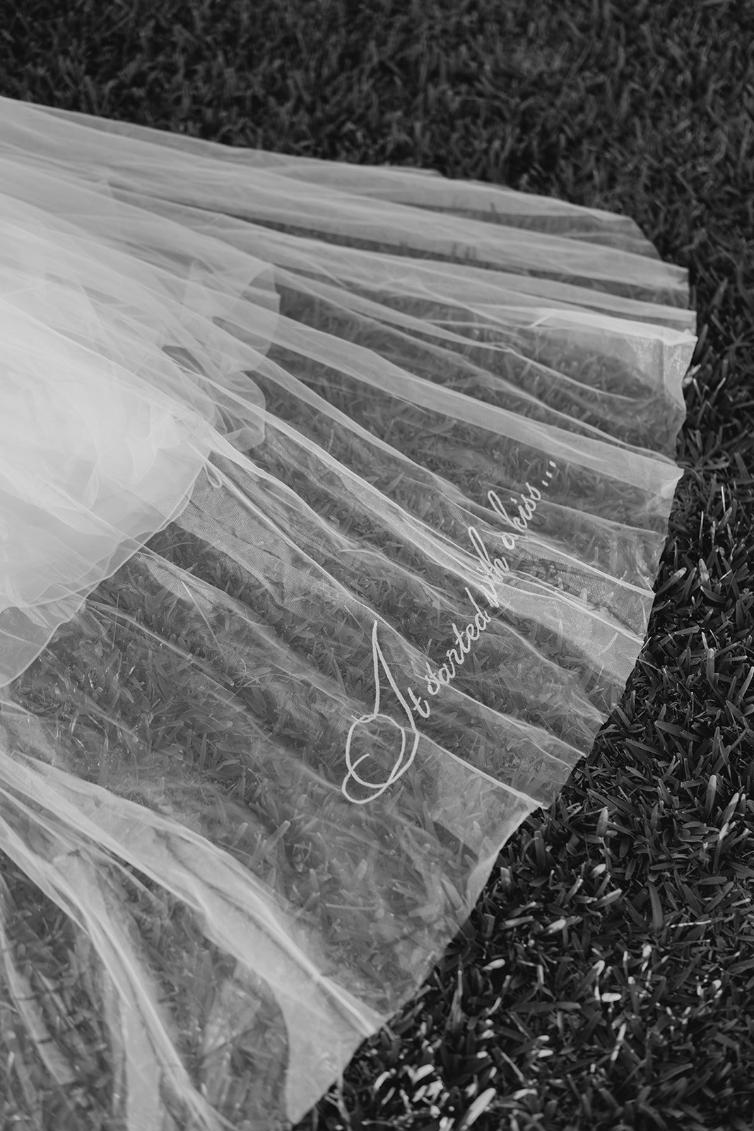 A wedding veil with embroidered text lying on grass