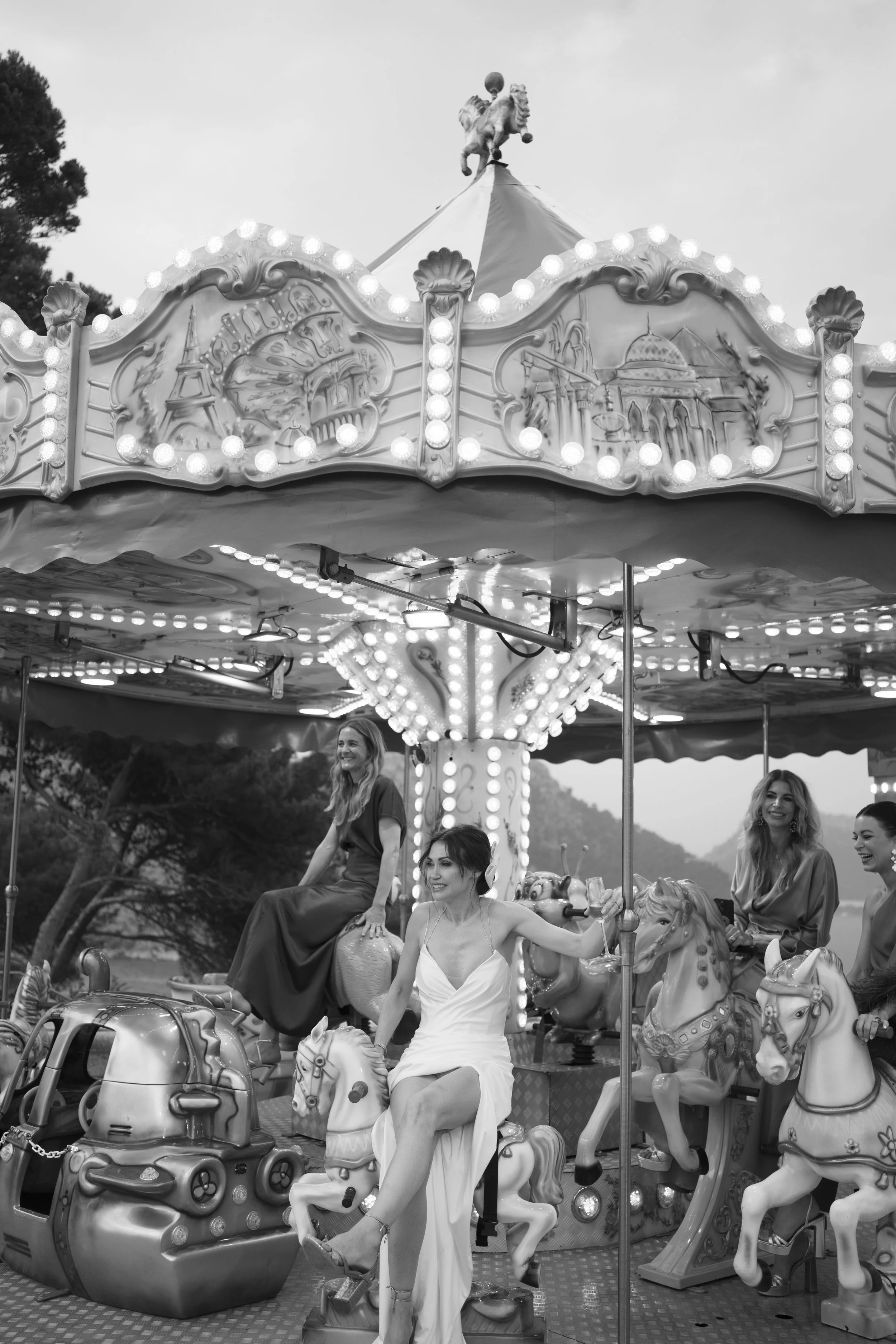 Four women enjoying a carousel ride at an amusement park, with trees and mountains in the background.