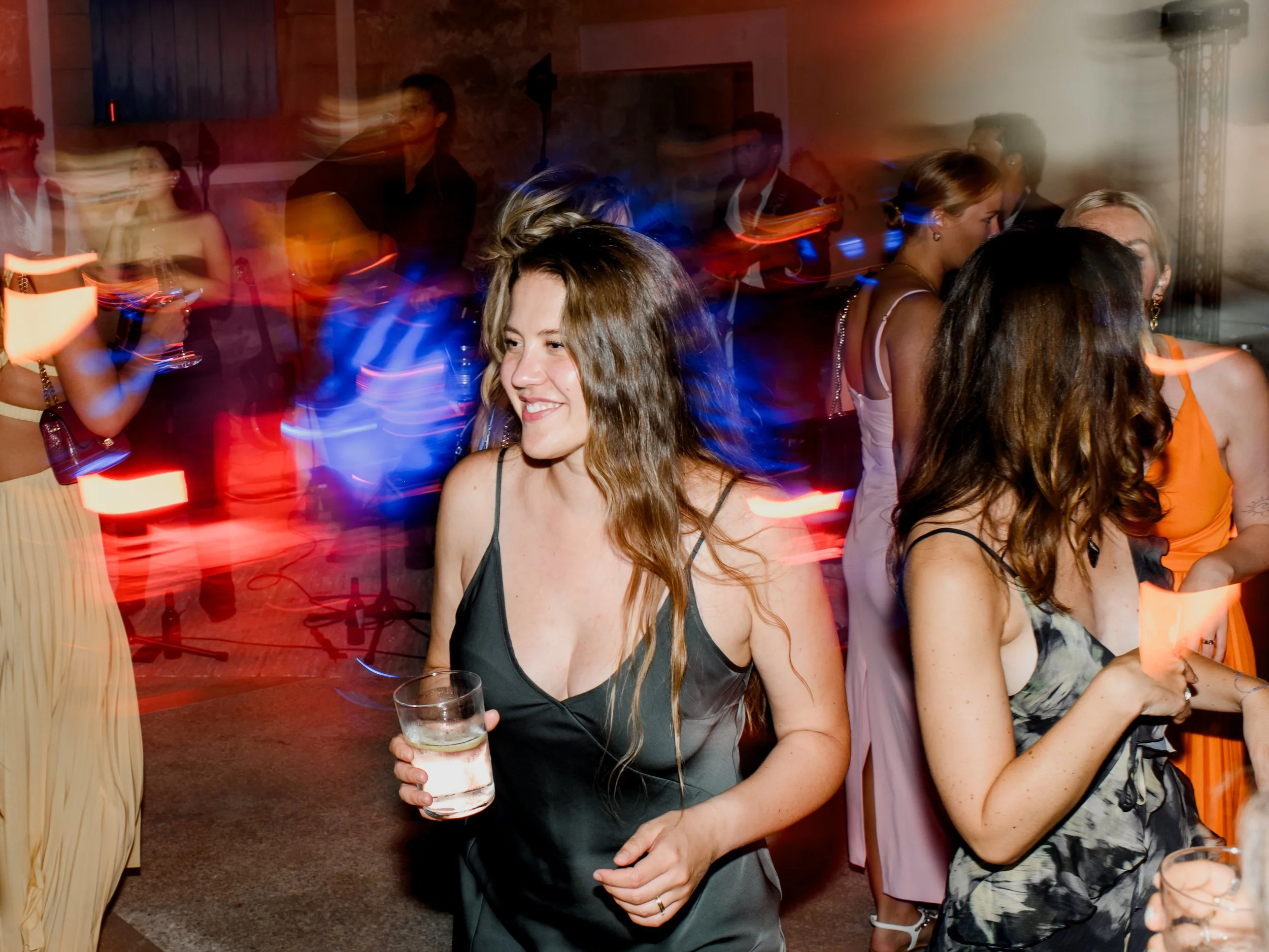 People dancing at a lively party, with colorful lights creating motion blur effects.