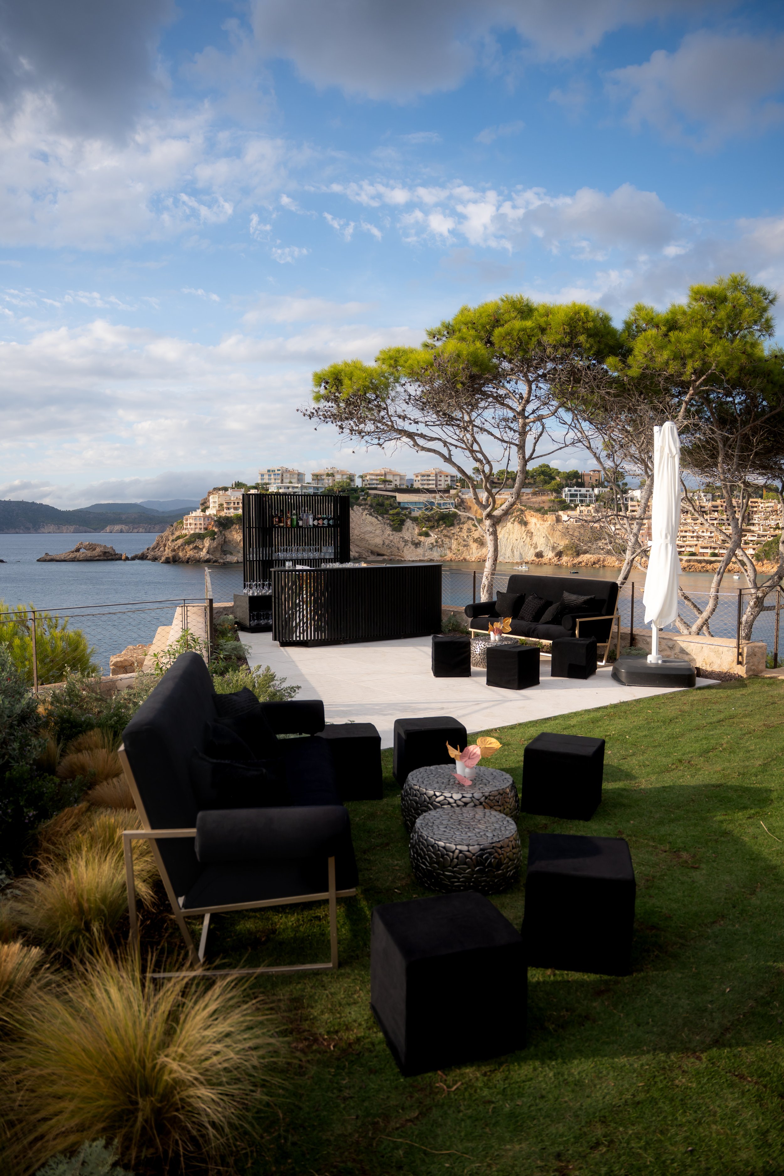 Outdoor patio overlooking water, with black furniture, trees, and a cloudy sky.