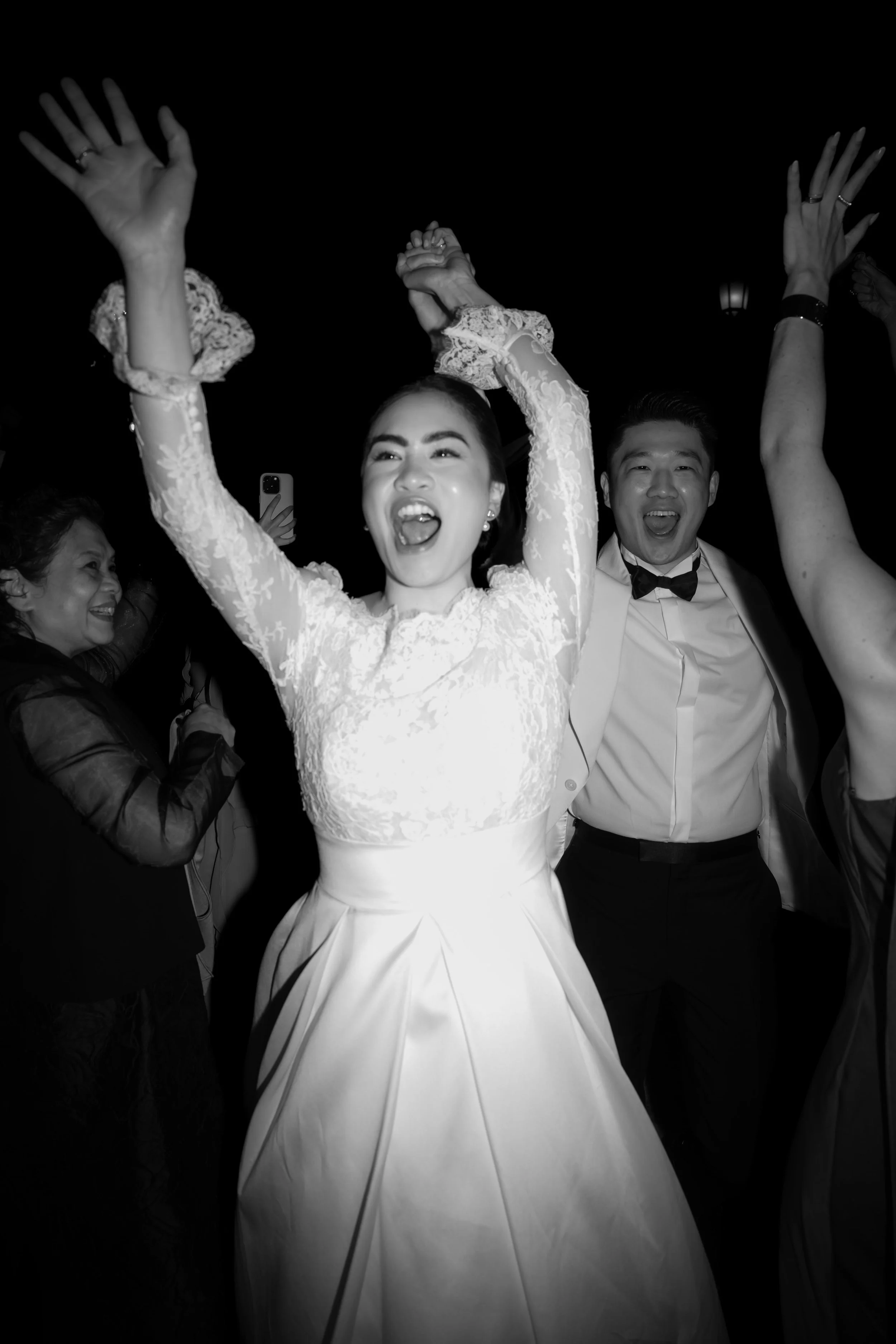Black and white photo of a bride in a wedding dress celebrating with friends at a wedding reception.