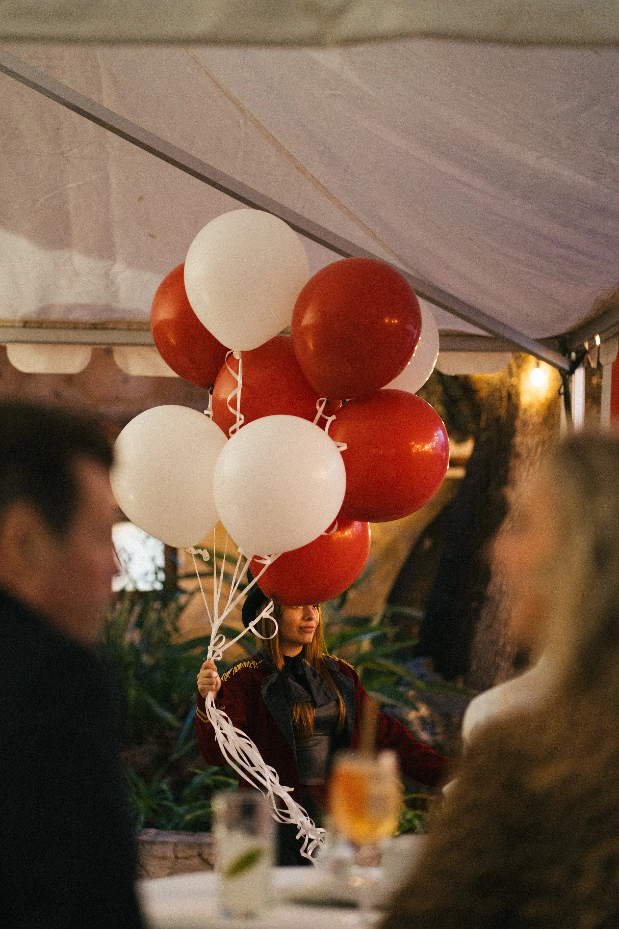A woman holding a bunch of white and red balloons at an outdoor event during the evening.