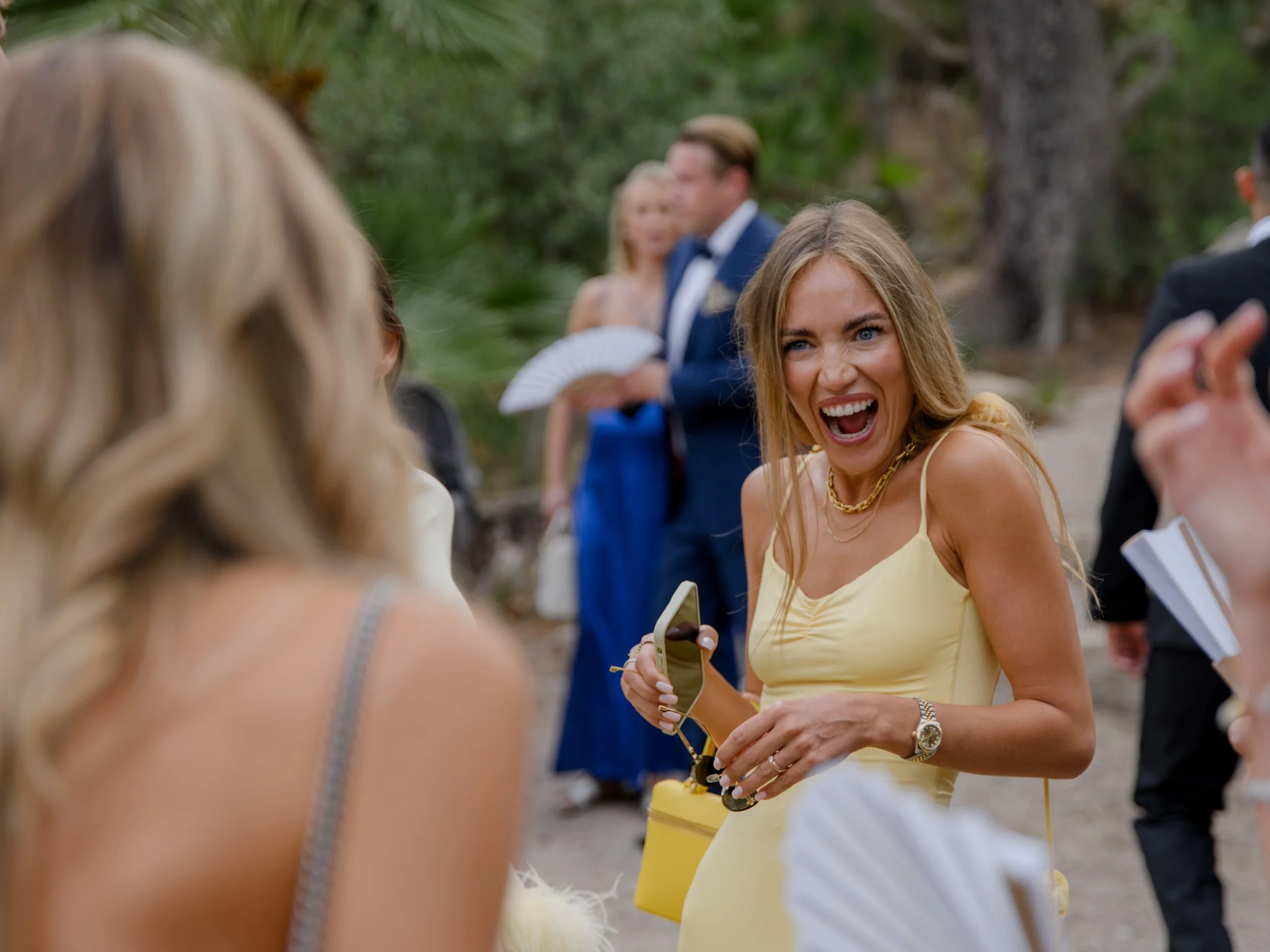 Woman in yellow dress laughing and holding sunglasses at outdoor event